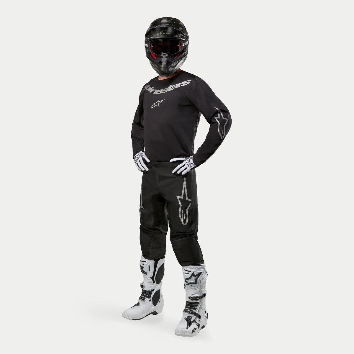 Motocrossförare i Alpinestars 2024 Fluid Graphite-tröja i svart och silver, matchande svarta byxor med silverfärgade stjärnlogotyper, vita och svarta stövlar, vita och svarta handskar, svart hjälm med röda goggles, komplett racingutrustning för terrängkörning