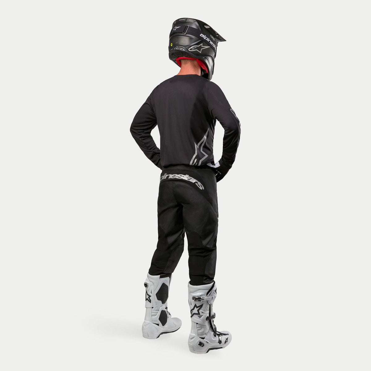 Motocrossförare bär Alpinestars 2024 Fluid Graphite Jersey i Black Silver sedd bakifrån, långärmad tröja med atletisk passform kombinerad med svarta motocrossbyxor, svart hjälm och vita och svarta stövlar, komplett professionell utrustning för terrängkörning