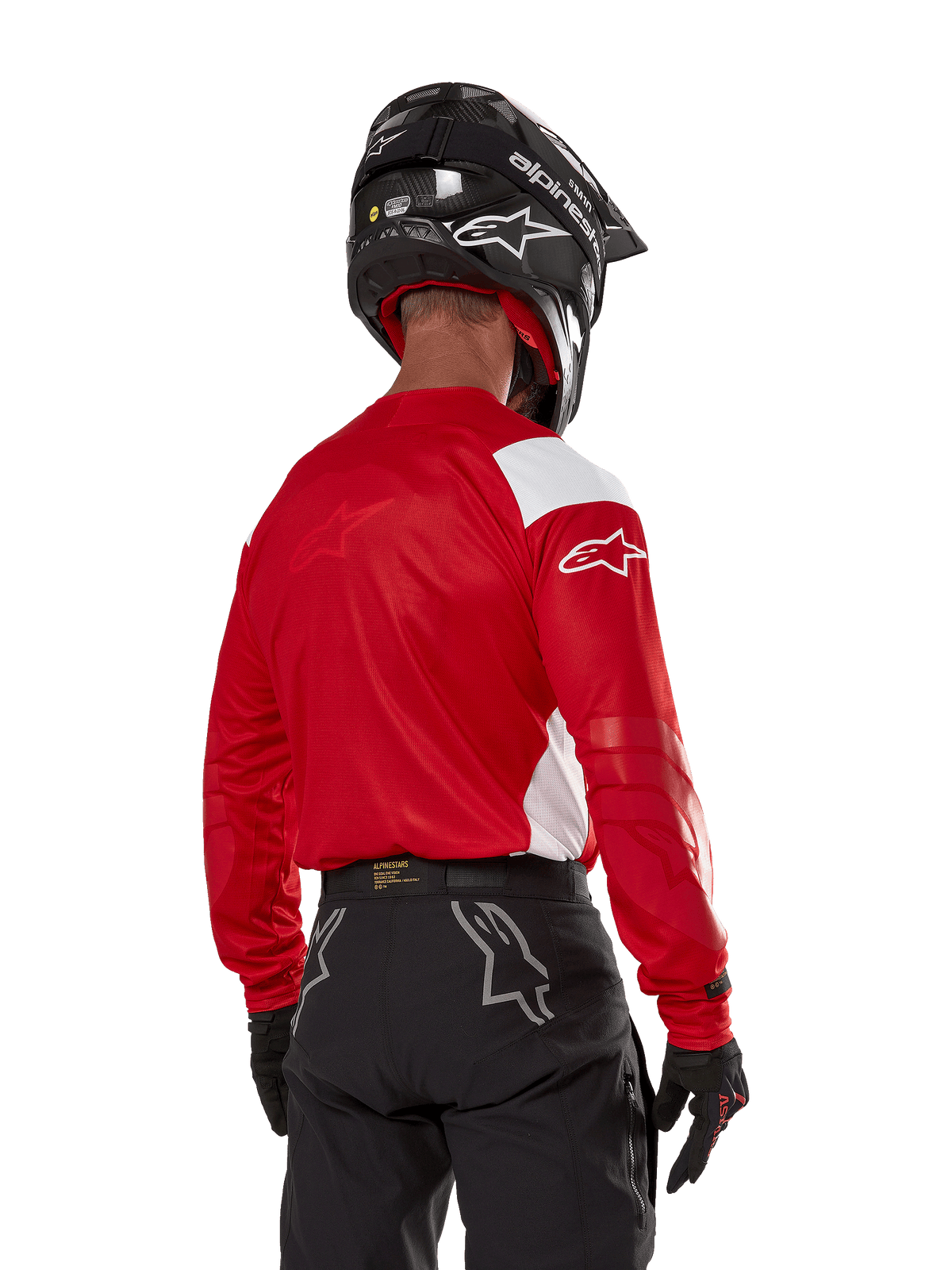 Motocrossförare sedd bakifrån bär Alpinestars Techdura Jersey i klarrött med vita paneler, kombinerat med svarta off-road-byxor, svart hjälm och svarta handskar, koordinerad utrustning för enduro- och motocrosskörning.