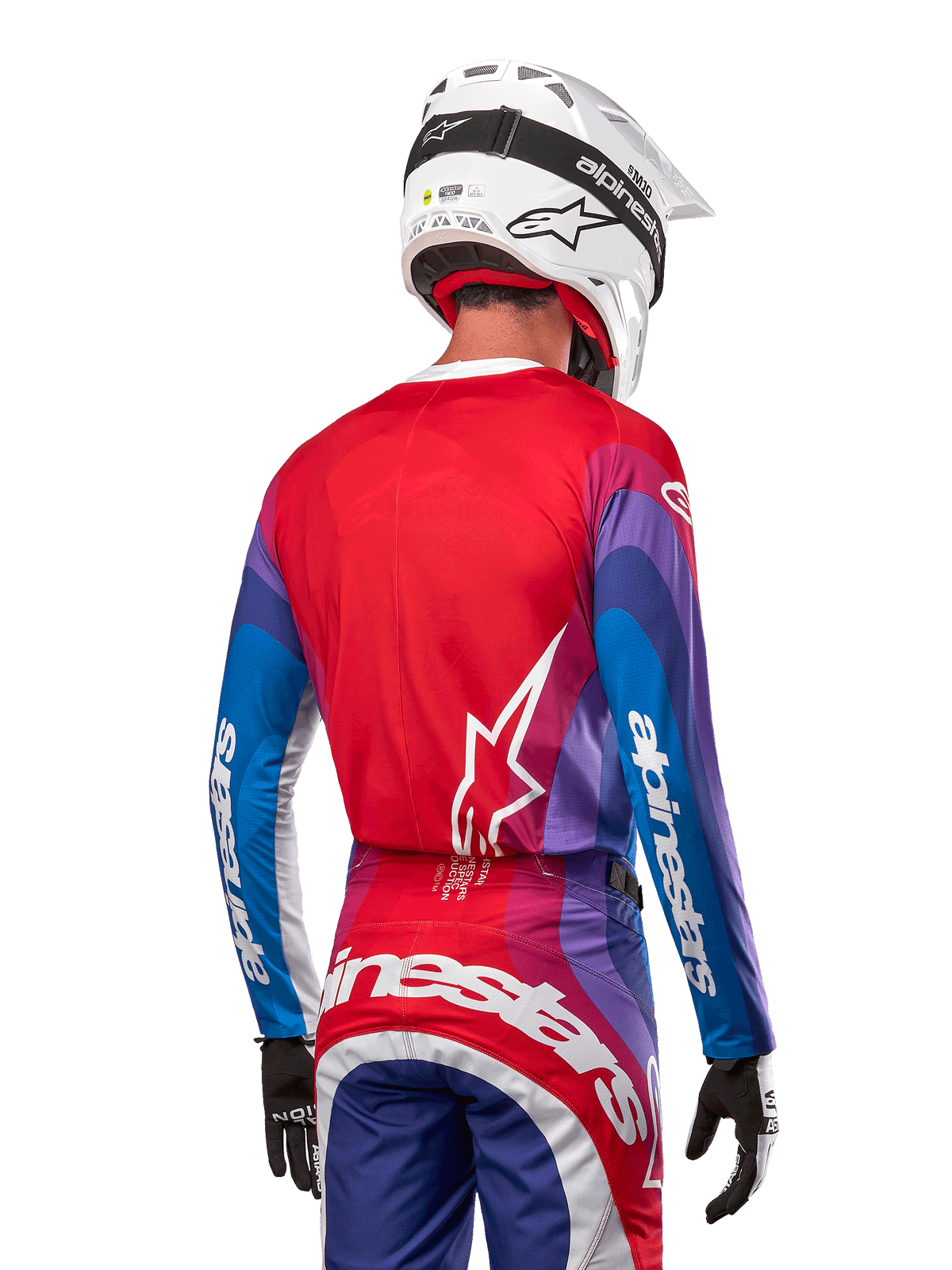 Motocrossförare sedd bakifrån i Alpinestars 2024 Techstar Pneuma Jersey i Blue Mars Red White, med röd rygg och vit stjärnlogotyp, blå och lila ärmar med vit logotyp, matchande byxor och vit hjälm för terrängkörning.