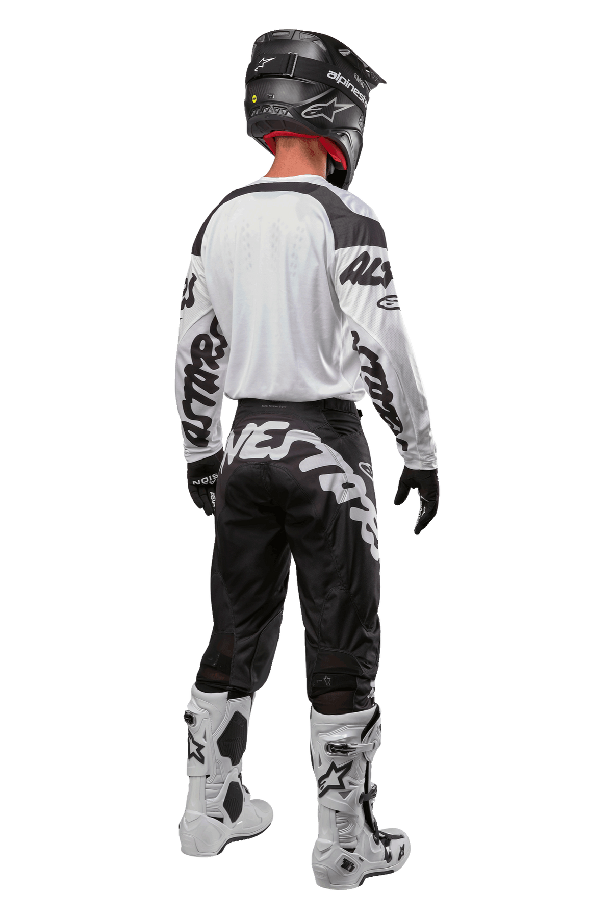 Alpinestars 2024 Racer Hana-tröja, ryggvy av motocrossförare, vit och svart, vit tröja med svart grafiskt tryck på ärmarna, matchad med svarta byxor med vit Alpinestars-text på sätet, svart hjälm och vita och svarta stövlar, koordinerad racingutrustning för terrängkörning