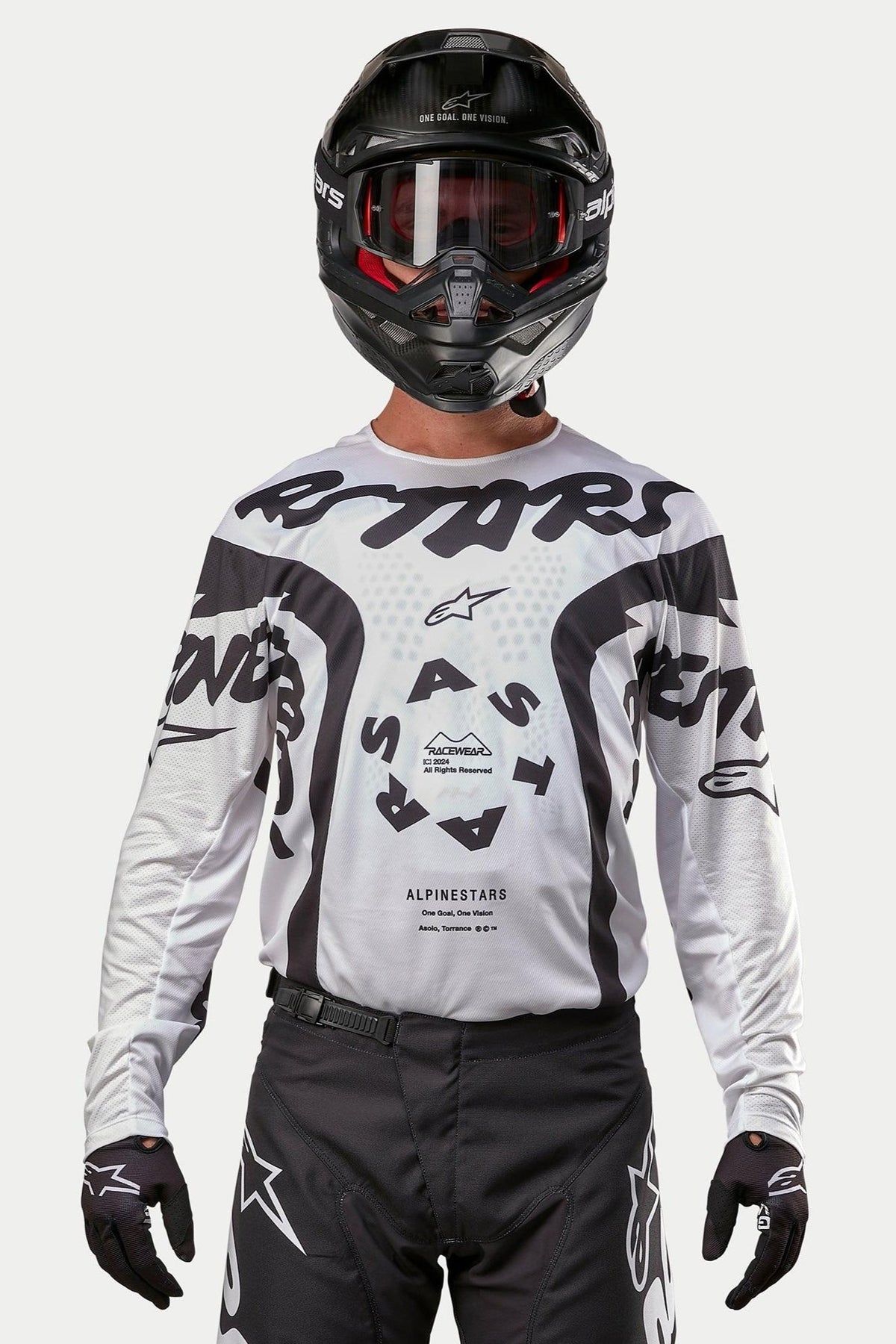 Motocrossförare som bär Alpinestars 2024 Racer Hana Jersey i vitt och svart, kombinerat med en svart hjälm och svarta motocrossbyxor, med framträdande svart 'ASTARS'-grafik och en cirkulär logotyp i mitten, professionell utrustning för terrängracing