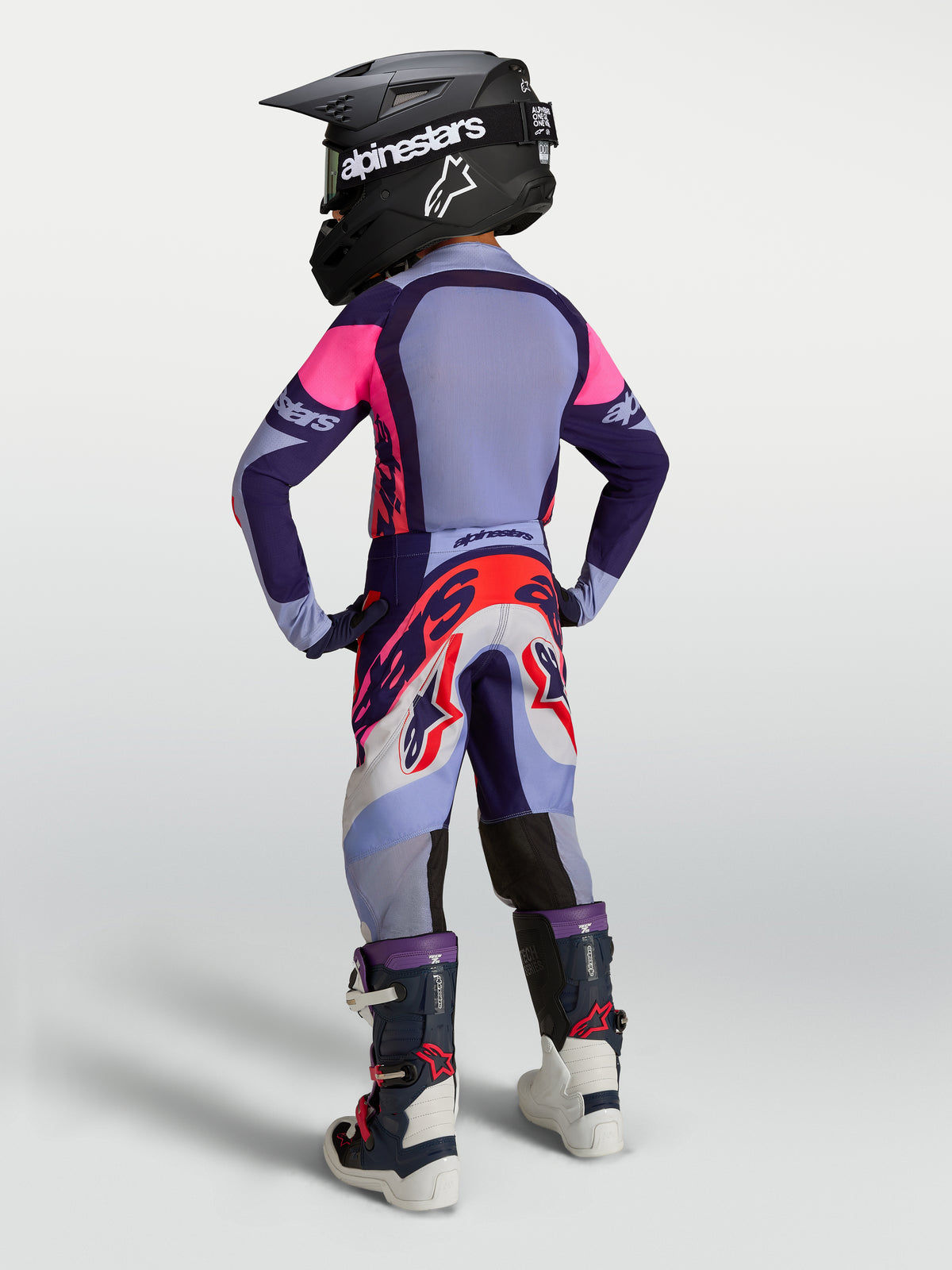 Alpinestars Ungdom Supertech Dyna Gear Set, lila och rosa motocrosskläder med tröja, byxor, hjälm och stövlar sedda bakifrån.