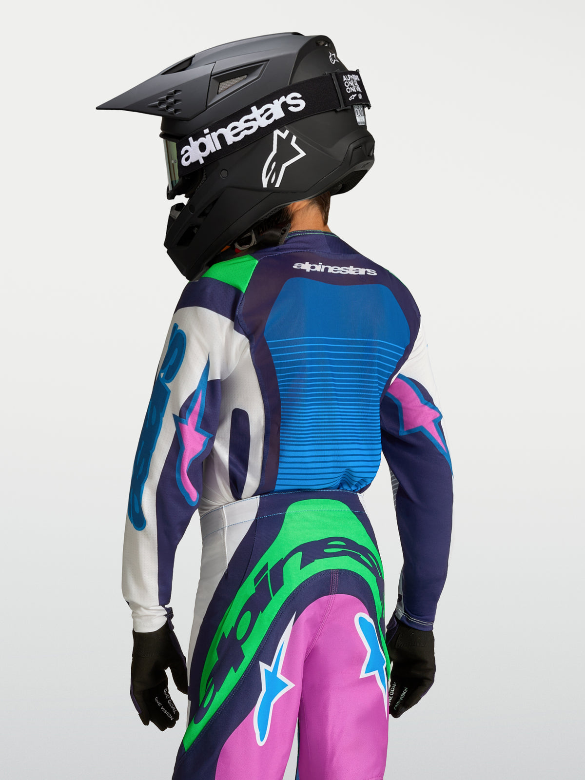 Alpinestars 2027 Supertech Maven ungdomströja, blå och grön motocrosströja, vy bakifrån med hjälm för terrängkörning.