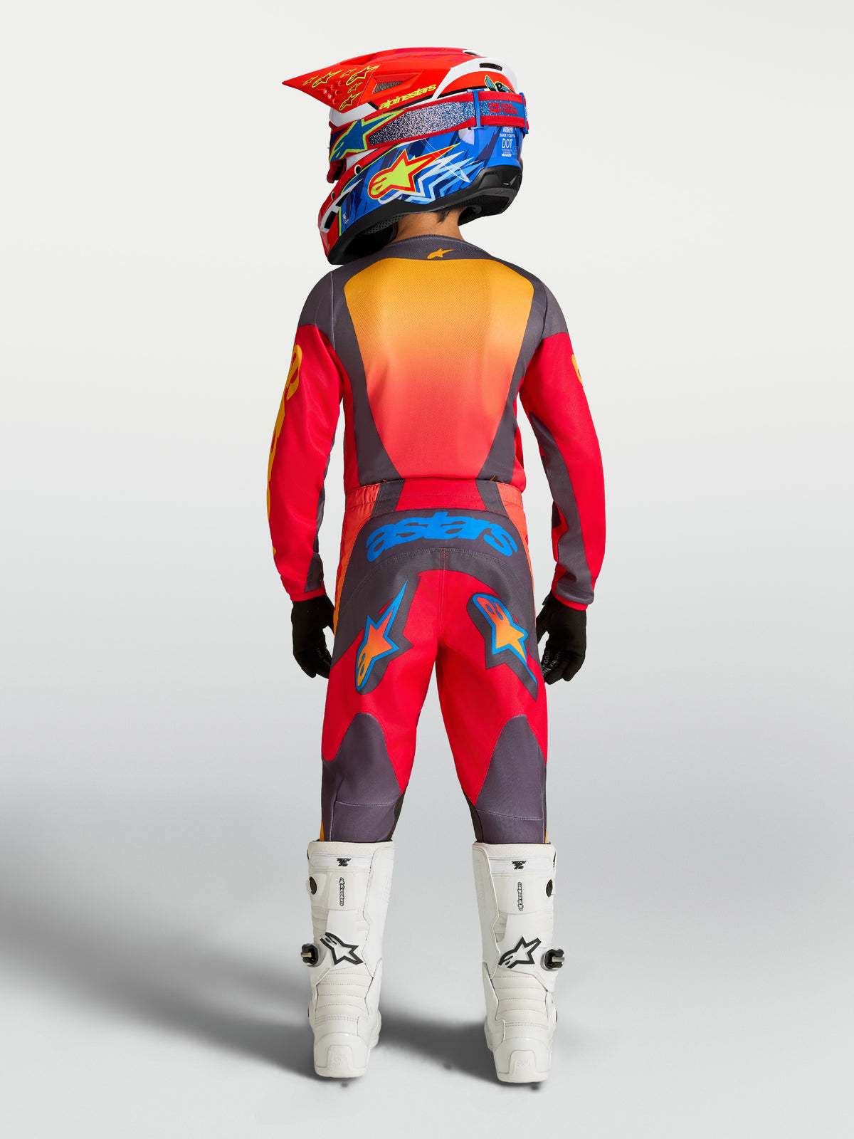 Alpinestars 2027 Ungdom Fluid Hunt-set, röd och grå motocrossutrustning sedd bakifrån på modell med vita stövlar.