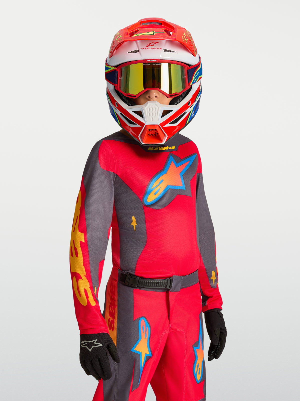 Alpinestars 2027 Fluid Hunt ungdomströja, röd och grå motocrosströja för ungdomar, fukttransporterande polytyg, bärs av modell med matchande hjälm och handskar för terrängkörning.