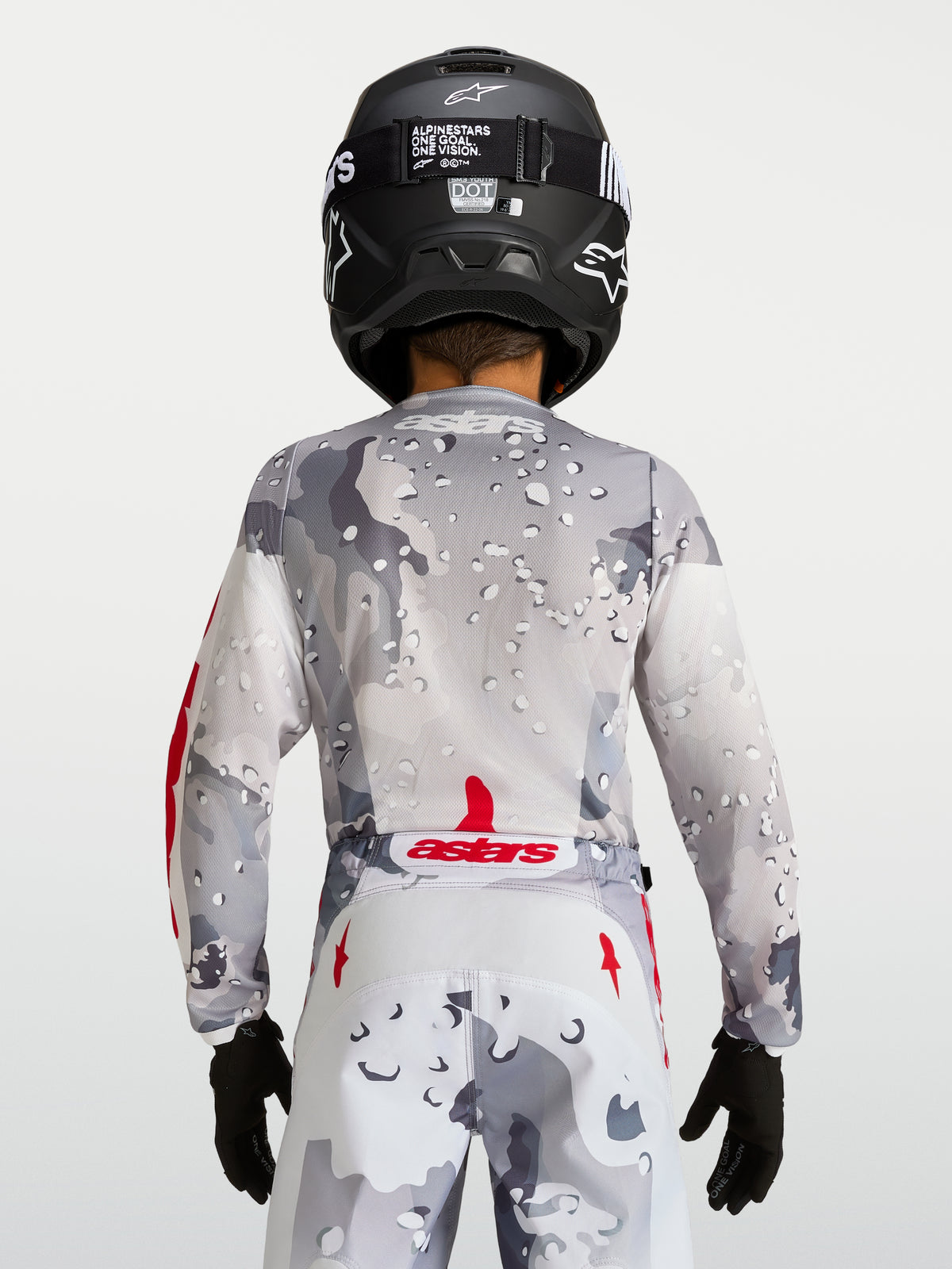 Alpinestars 2027 ungdom Fluid Lone tröja, grå kamouflagemönstrad motocrosströja, vy bakifrån, röda detaljer, svart hjälm.