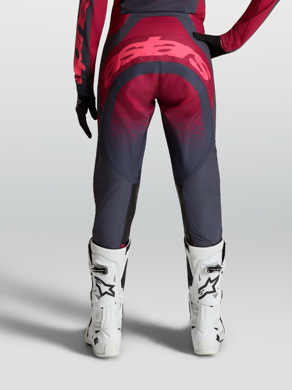Alpinestars Stella Techstar Swan Byxor, dambyxor för motocross, grå och röda, vy bakifrån på modell med vita tävlingsstövlar, hållbar 600D-polytygskonstruktion och förstärkt sätesområde.
