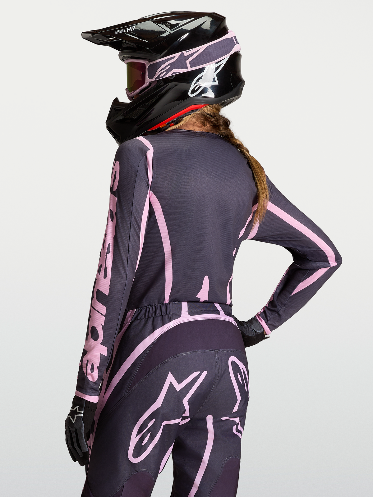 Alpinestars Stella Fluid Apex V2 damtröja för motocross, grå och rosa, bärs av modell bakifrån med matchande byxor och svart hjälm.
