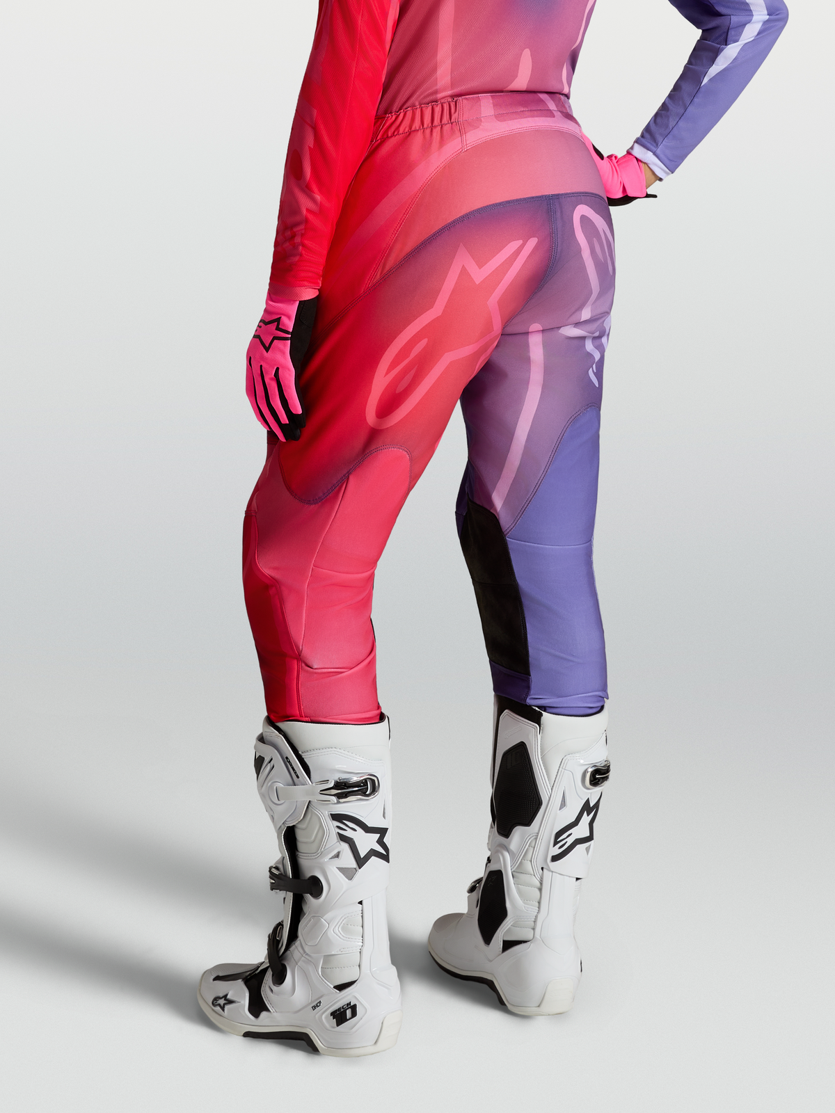 Alpinestars Stella Fluid Kepler byxor, motocrossbyxor för dam, lila och röda, vy bakifrån med förböjda ben och stretchpaneler, på modell med vita Tech 10 stövlar.
