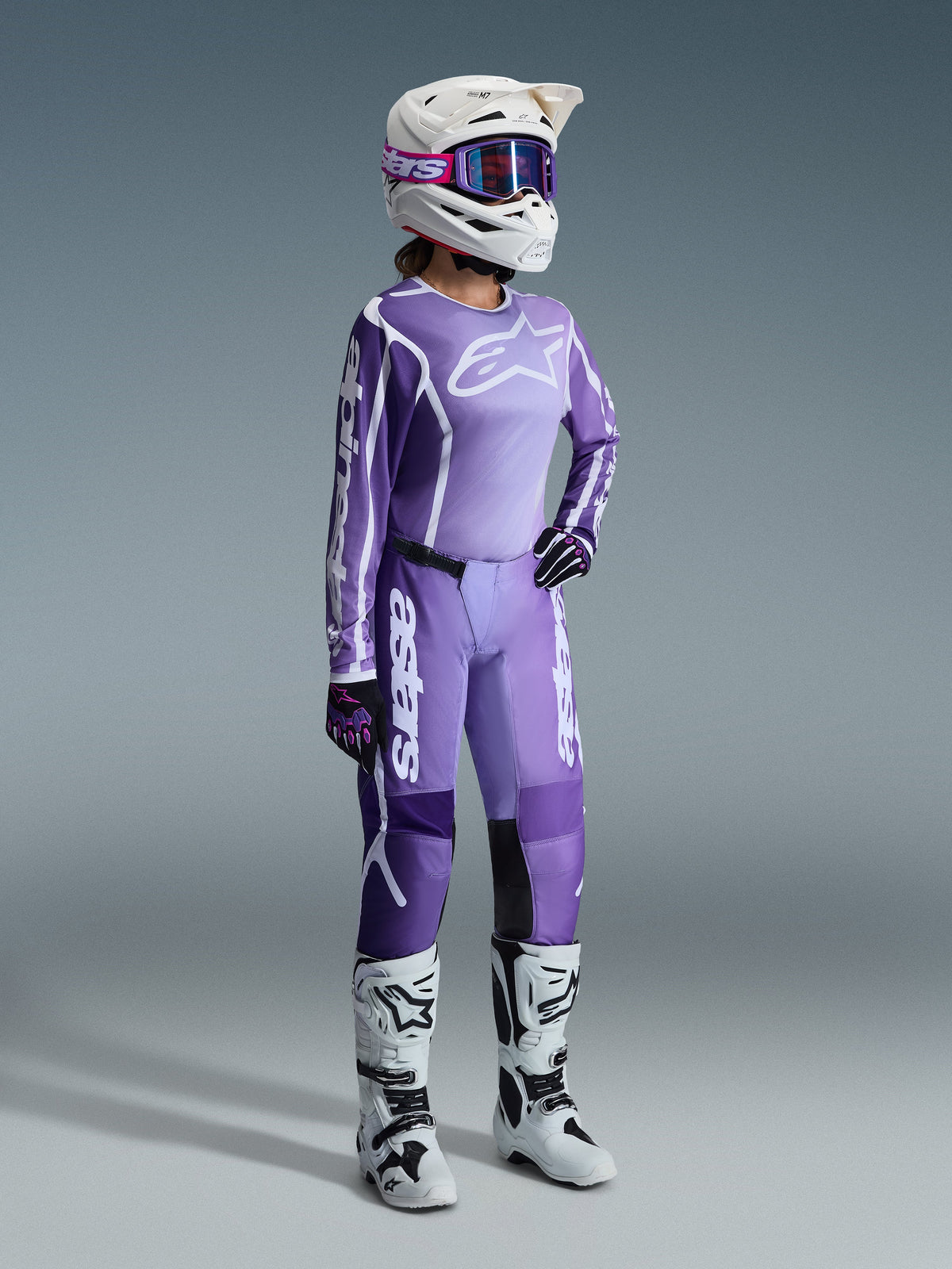 Alpinestars 2026 Stella Fluid Apex Gear Set, lila och lavendel, kvinnlig motocrossförare i matchande tröja och byxor, vit hjälm med lila goggles, vita och svarta stövlar, svarta och lila handskar, komplett högpresterande outfit för terrängkörning för damer