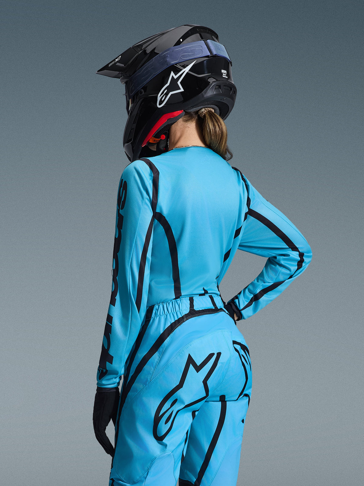 Alpinestars 2026 Woman Stella Fluid Apex Gear Set, Light Blue with black curved graphics, viewed from behind on a female rider, worn with a black helmet and gloves, ergonomic women's motocross apparel