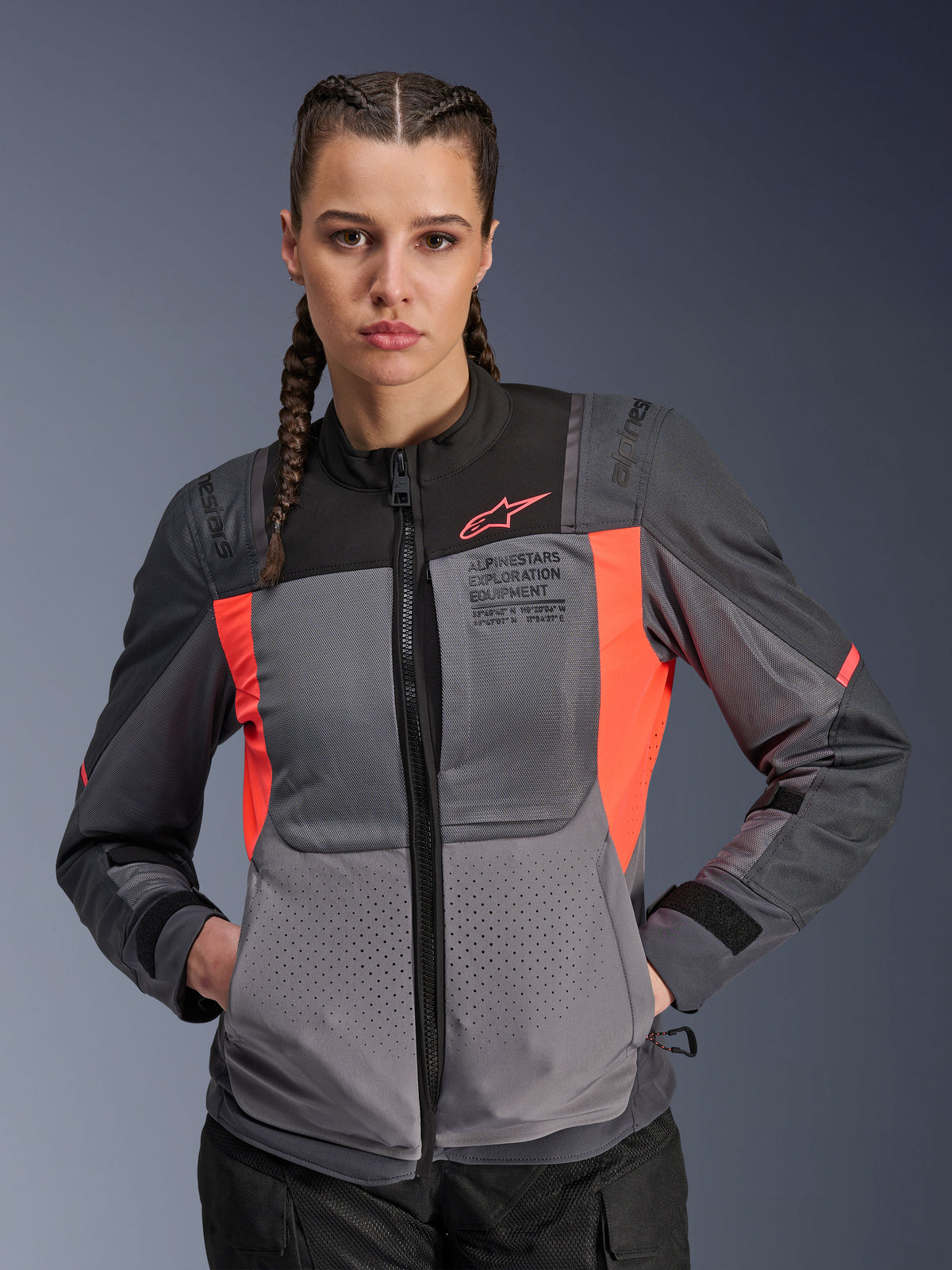 Alpinestars Stella ST-2 Air jacka, motorcykeljacka för dam, mörkgrå och Fluo Coral, bärs av modell med flätat hår, med tekniska meshpaneler för luftflöde, laserperforeringar och 'Alpinestars Exploration Equipment'-märkning på bröstet, sommar-touringutrustning