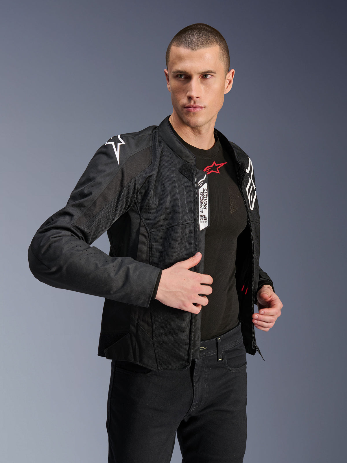 Alpinestars Viper Air V4-jacka, svart motorcykeljacka i textil, bärs av en manlig modell med svarta jeans och underställ, öppen framtill med synliga Tech-Air Ready- och Alpinestars Protects-etiketter, vita logotyper på axlarna, meshpaneler för luftflöde