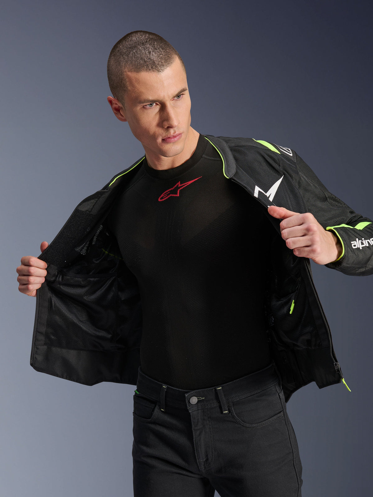 Manlig modell i Alpinestars T-Sps Air V2-jacka i svart och gul fluo, visas öppen för att framhäva den inre meshkonstruktionen och fickorna, matchad med ett svart Alpinestars-baslager och svarta byxor, urban motorcykelstil