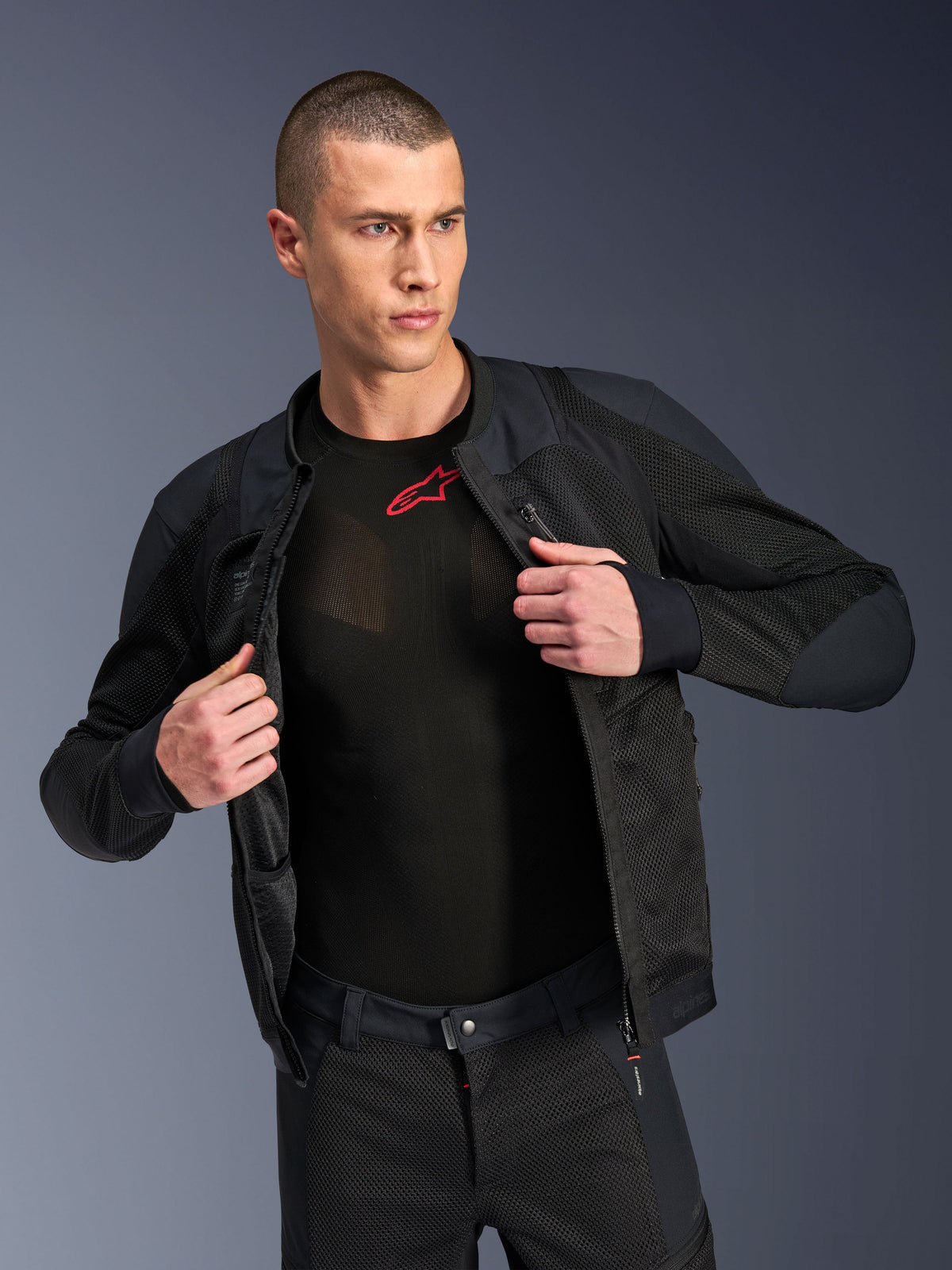 Alpinestars Troop-Air Pro-jacka, svart, teknisk bepansrad luftjacka i premiumutförande med meshkonstruktion, bärs öppen över ett svart baslager med röd logotyp, kombinerad med matchande motorcykelbyxor i mesh, urban modern körstil
