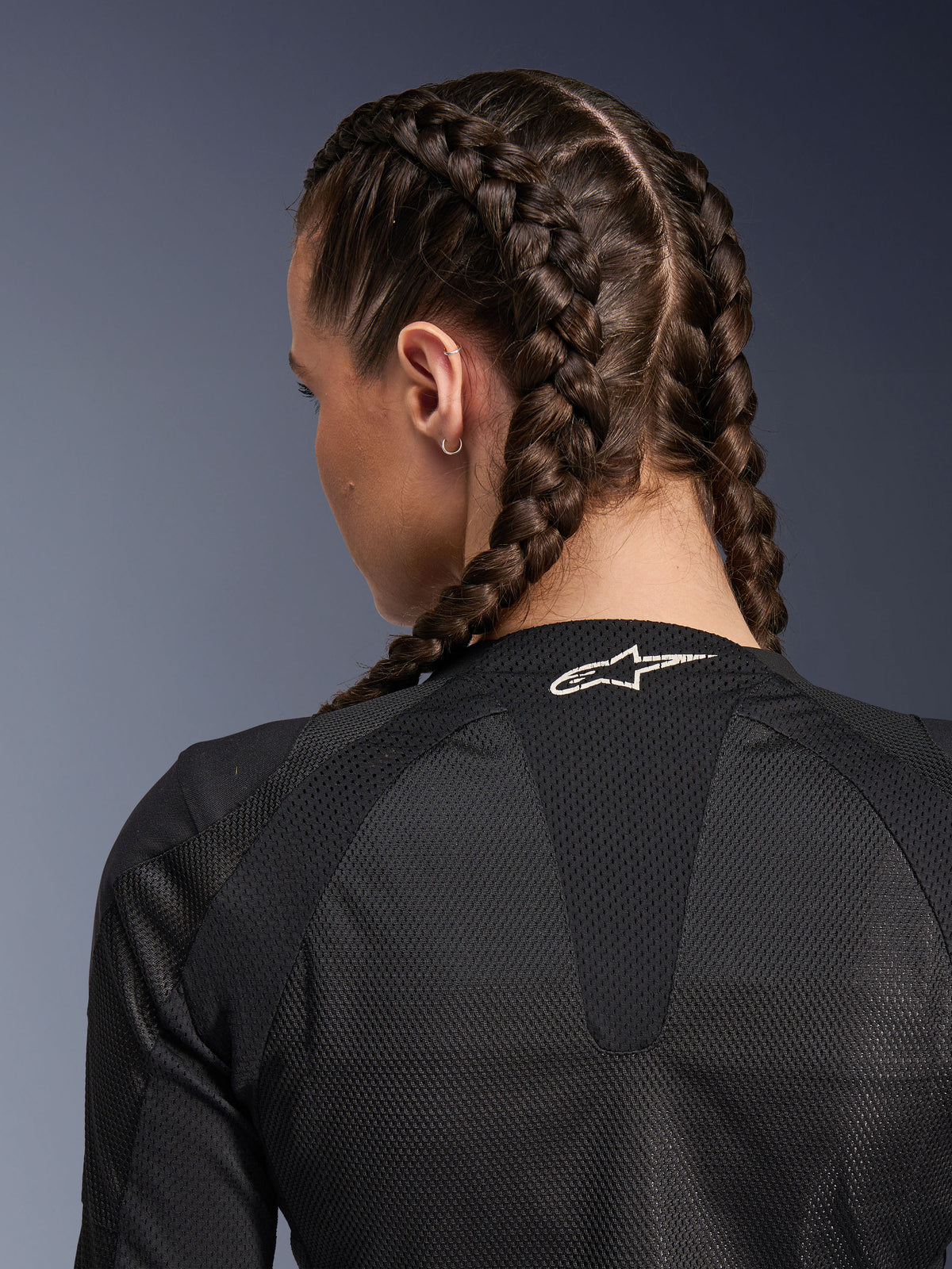Alpinestars Stella Troop-Air jacka för dam, svart, detaljerad vy bakifrån av övre rygg och nacke, kvinna med inbakade flätor, med en vit Astars-logotyp på kragen och lätt 2D-tech-mesh-material för ventilation