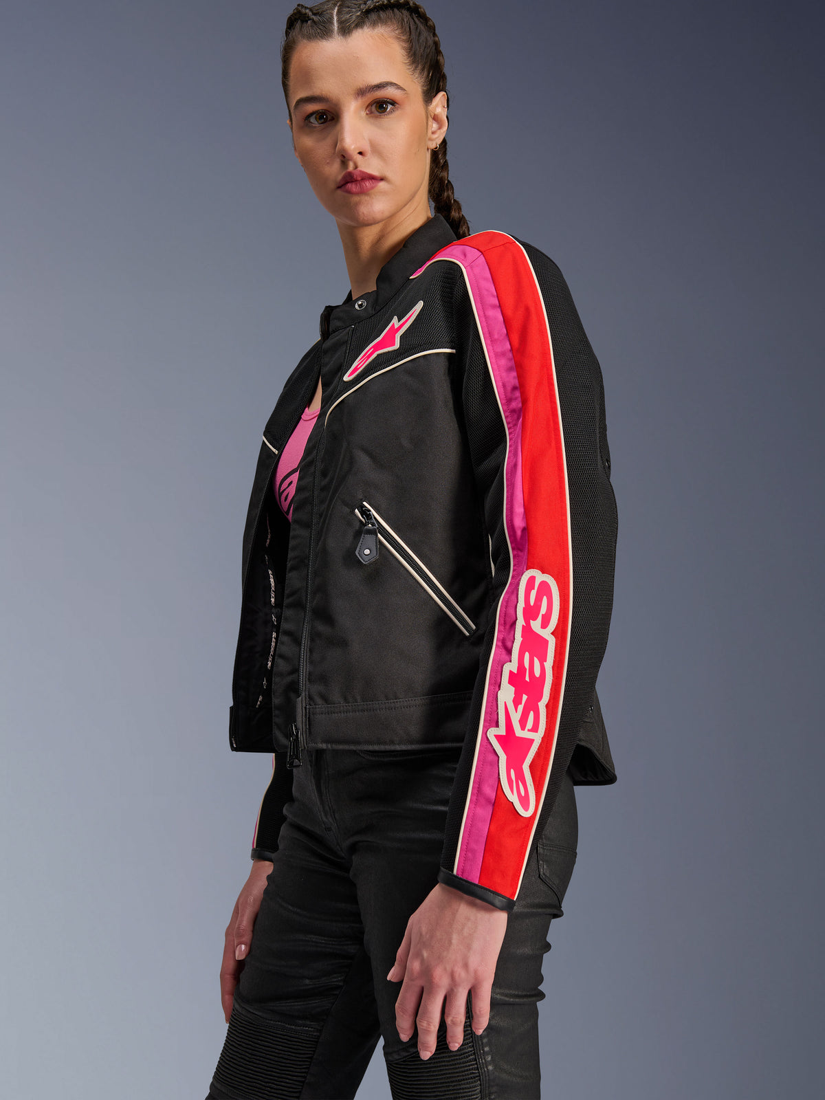 Alpinestars Stella T-Dyno Air motorcykeljacka för damer, svart med detaljer i klarrött och fuchsia, bärs med svarta byxor, rosa Astars-logotyp på bröstet och ärmen, skräddarsydd biker-passform med meshpaneler för ventilation