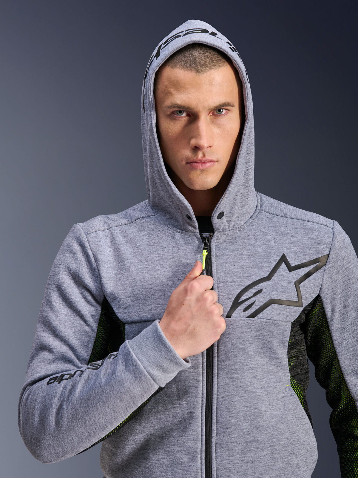 Alpinestars Chrome Air Sport Hoodie, Gray Heather Black, motorcykelhoodie som bärs av en man med huvan uppe, med en svart stjärnlogotyp på bröstet, neongul dragtapp och sidopaneler i mesh för ventilation, urban körstil