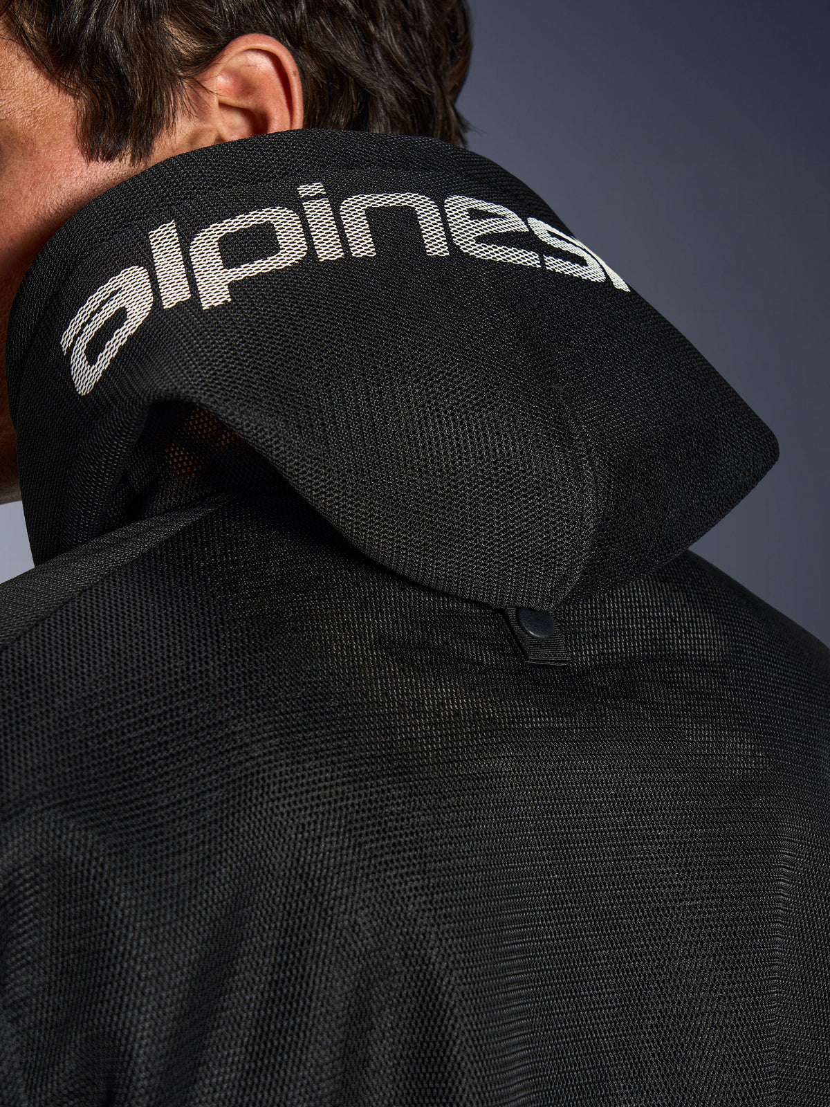 Alpinestars Chrome Superairflow Hoodie, svart, närbild av huvan i 3D-mesh med vit Alpinestars-logotyp längs toppen, visar den bakre stabiliseringstryckknappen, ventilerad mc-utrustning i textil för extrem värme