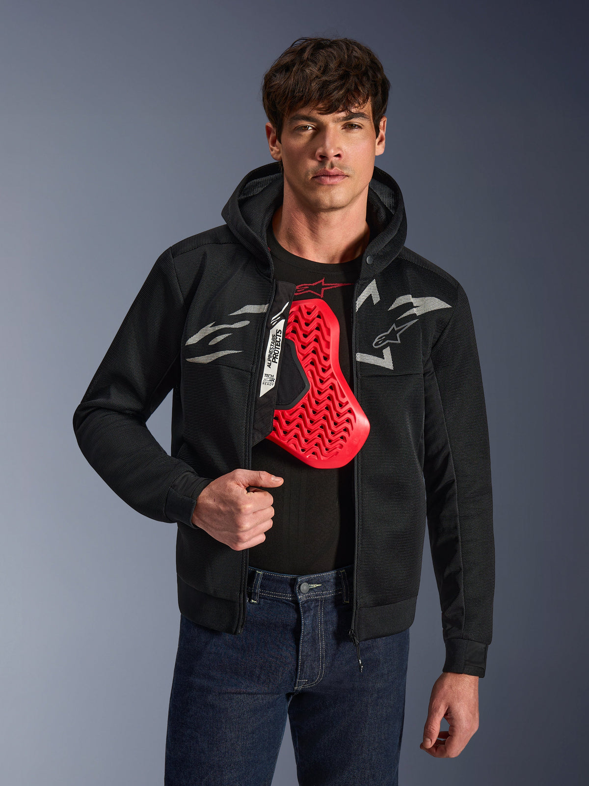 Alpinestars Chrome Superairflow Hoodie i svart, med vita och grå Astars-logotyper, bärs av en manlig modell med ett rött bröstskydd synligt undertill, 3D-mesh-textil för ventilation, sportig urban motorcykelutrustning.