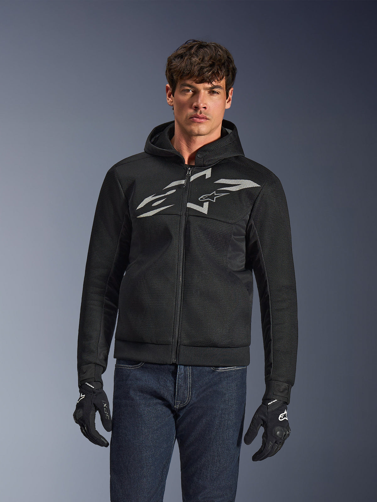 Alpinestars Chrome Superairflow Hoodie, svart motorcykelhoodie med dragkedja, stor vit logotyp på bröstet, ventilerande meshkonstruktion, bärs med blå jeans och svarta handskar, sportig urban MC-utrustning