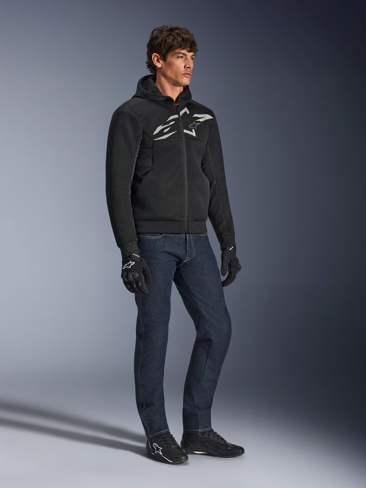 Alpinestars Chrome Superairflow Hoodie, svart med vit och grå logotyp, ventilerad 3D-mesh-textilkonstruktion, buren med mörkblå denimjeans och svarta motorcykelhandskar, urban sportig körstil.