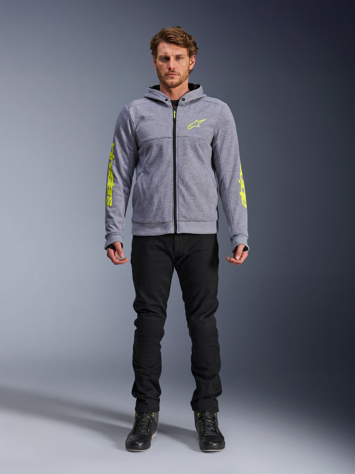Alpinestars Chrome V2 Sport jacka med huva, urban motorcykeljacka för herr, grå och fluorescerande gul, teknisk fleece med aramidförstärkningar, visas på modell med svarta byxor.