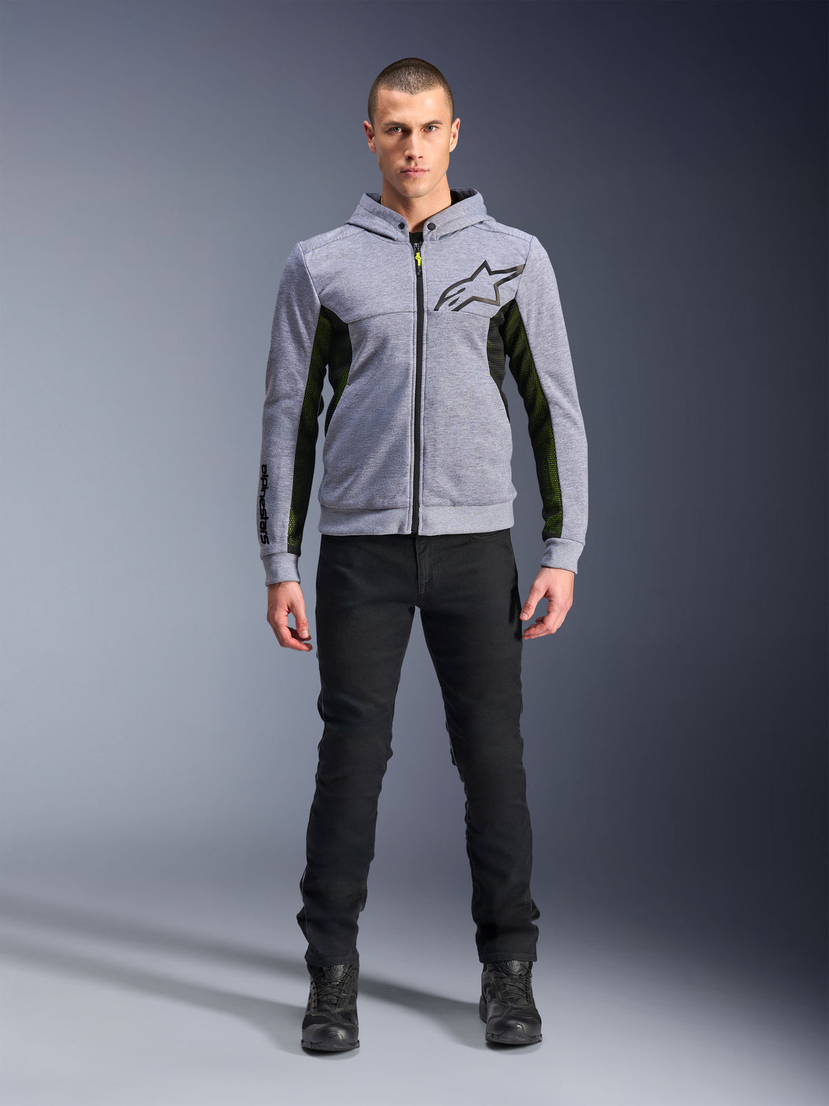 Alpinestars Chrome Air Sport Hoodie, gråmelerad svart, teknisk motorcykelhoodie med svarta mesh-sidopaneler och neongula detaljer, svart stjärnlogotyp på bröstet, bärs med svarta byxor och stövlar, modern urban körstil