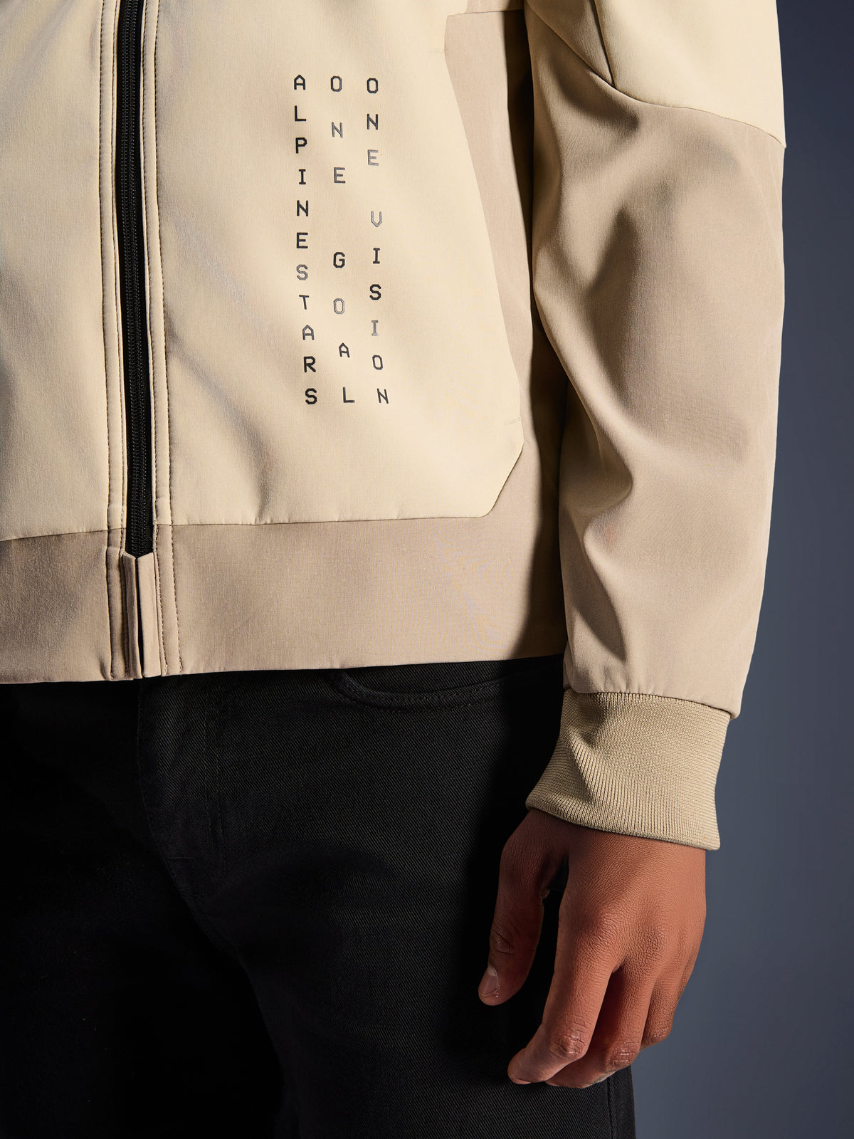 Alpinestars Radium Tech Hoodie i Mastic Aluminum, närbild av bröst och ärm, vertikal svart textlogotyp 'Alpinestars One Goal One Vision', ribbad stretchmudd och dragkedjedetalj, urban mc-textiljacka