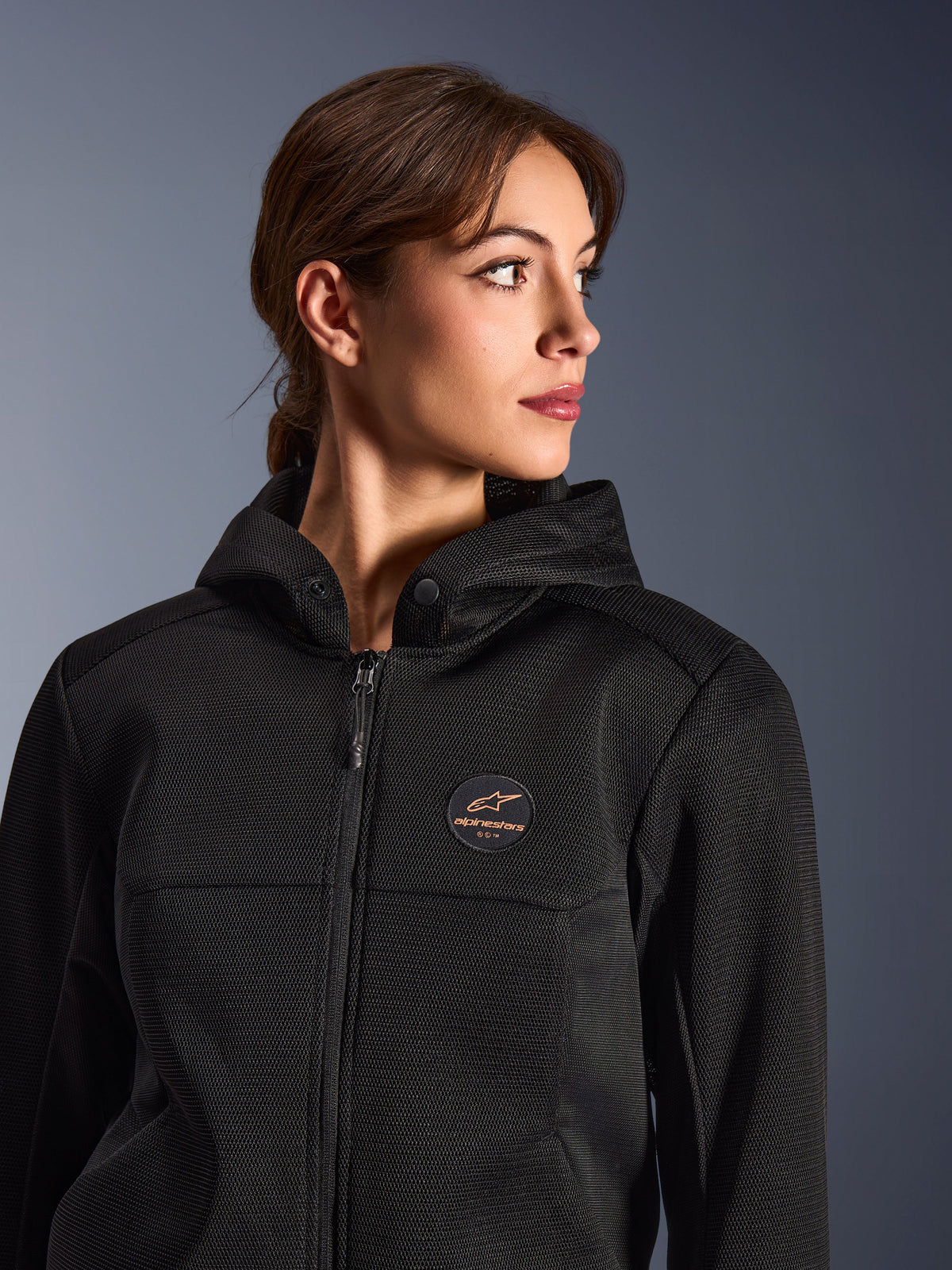 Woman wearing the Alpinestars Stella Chrome Superairflow Hoodie, Black with copper logo, 3D mesh construction for maximum airflow, technical motorcycle gear designed for women, urban sport riding style