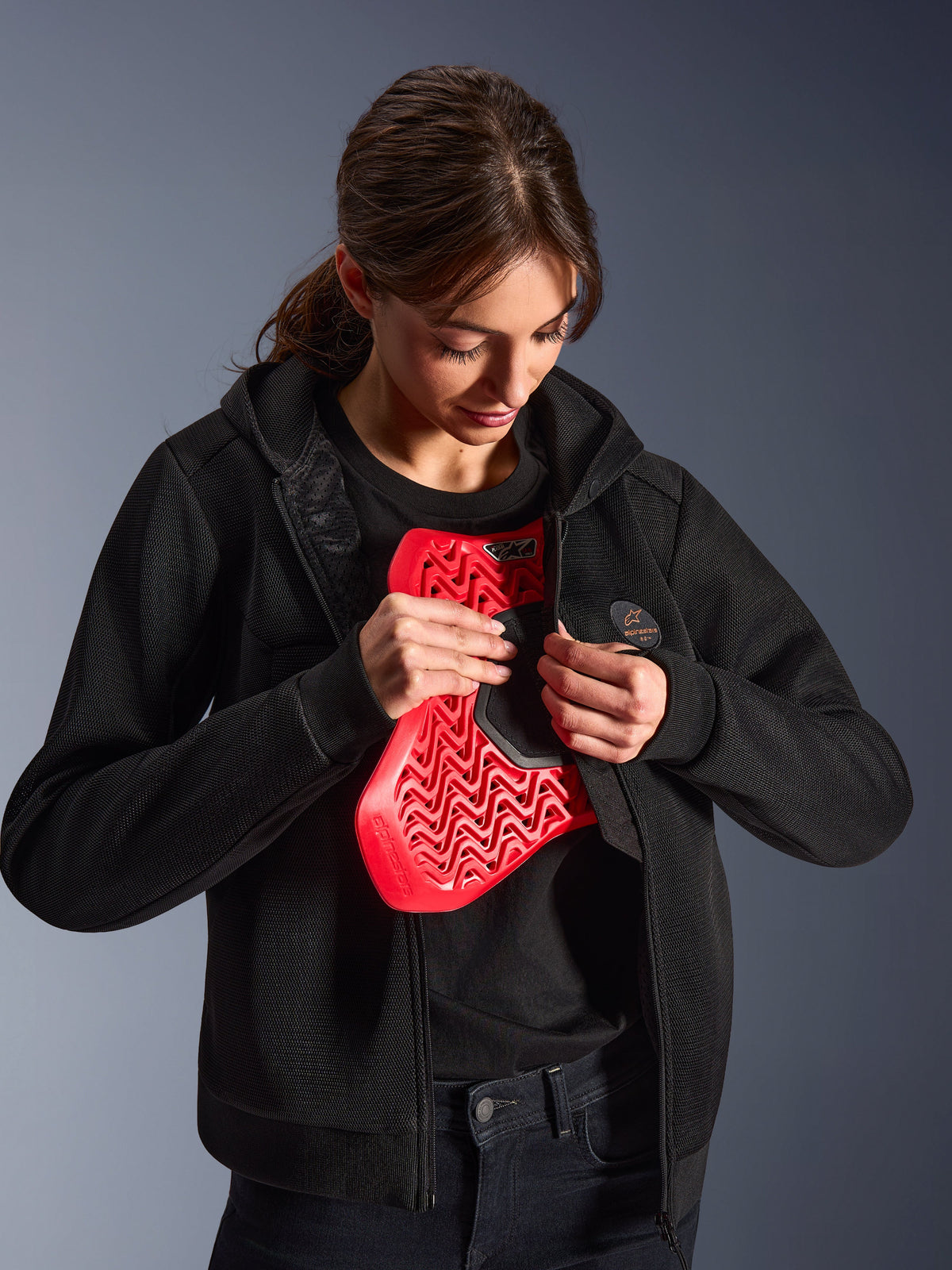 Alpinestars Stella Chrome Superairflow Hoodie, Women's Motorcycle Hoodie, Black, model holding a red Nucleon chest protector, lightweight 3D mesh construction for urban and sport riding
