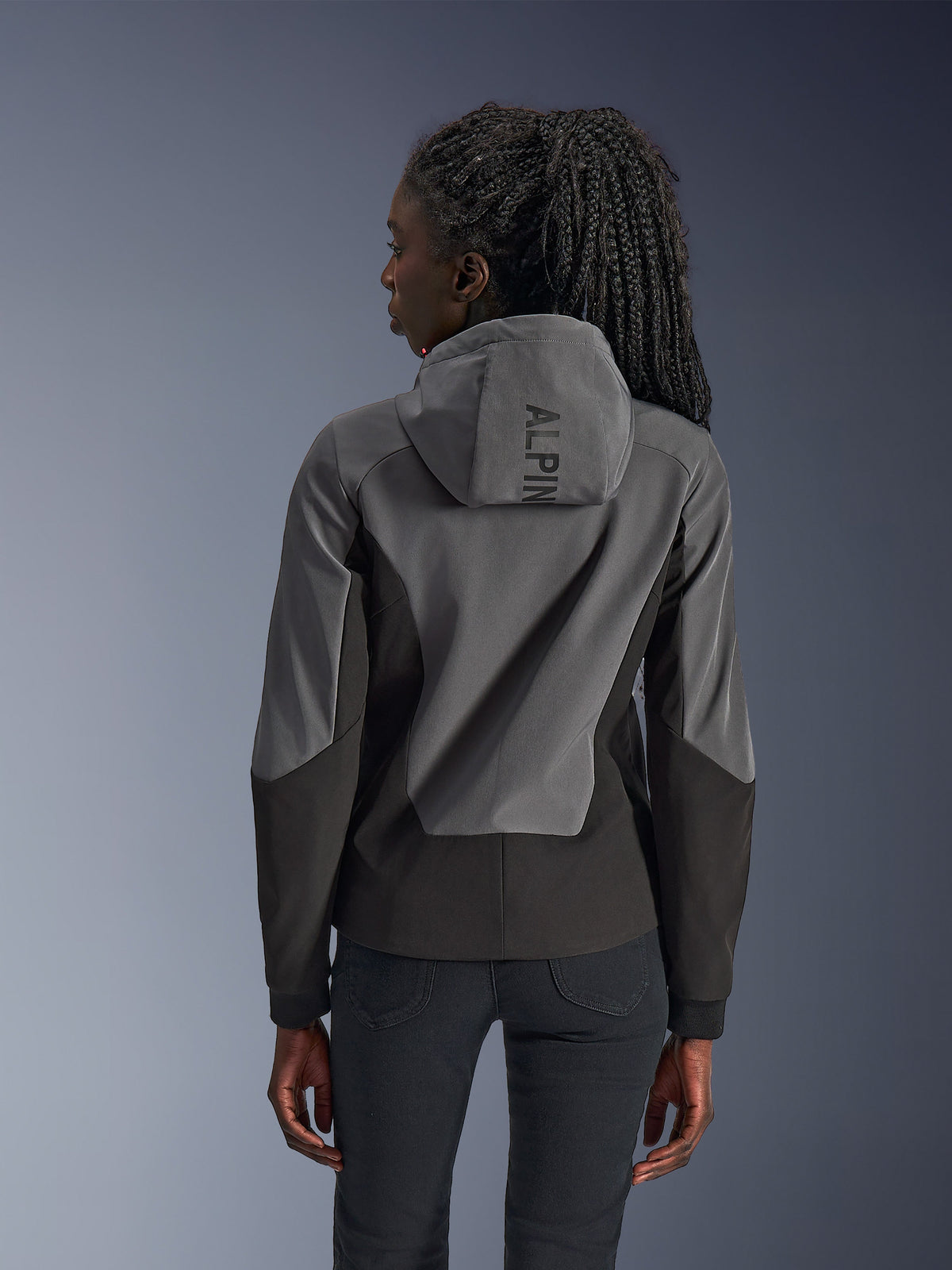 Kvinna i Alpinestars Stella Radium Tech Hoodie, vy bakifrån, Deep Gray Black, tvåtonat grått och svart 3-lagers vindtätt skal, Alpinestars-logotyp på huvan, urban motorcykeltröja med atletisk passform