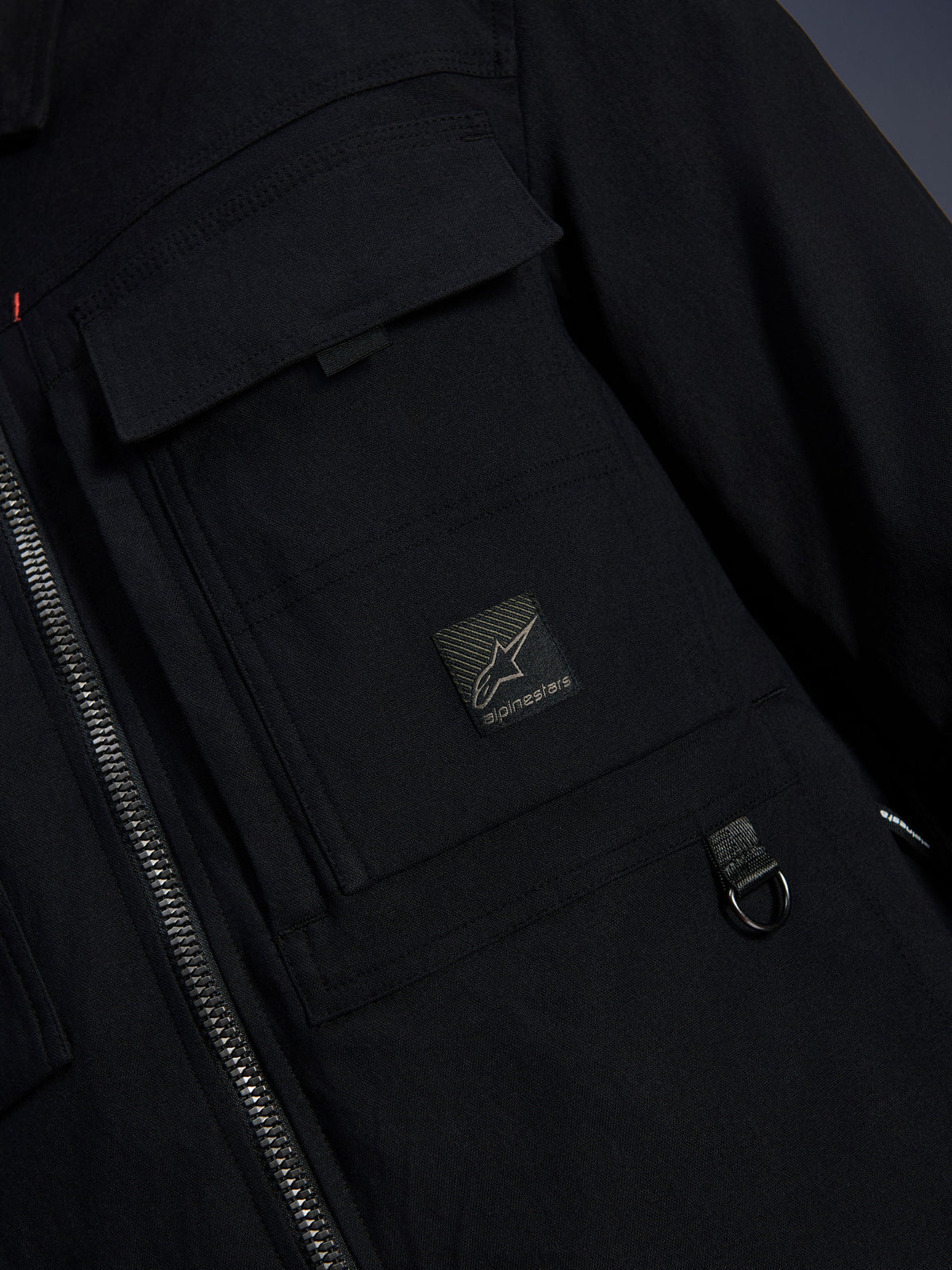 Alpinestars Bryon Water Resistant Overshirt, svart, närbild på vaxat canvastyg, främre dragkedja, bröstficka av cargomodell med Alpinestars logotypmärke och detalj med D-ring i metall