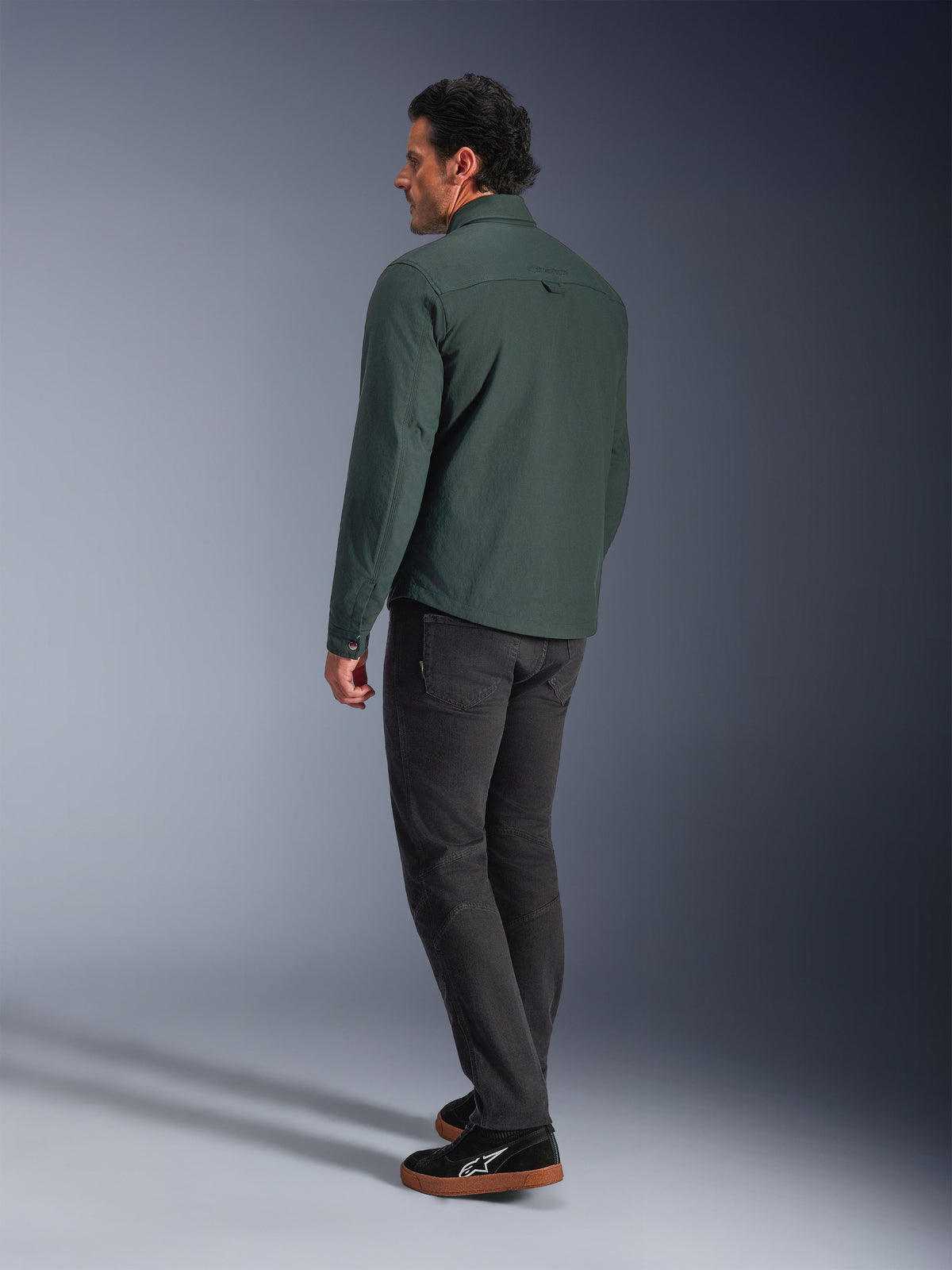 Alpinestars Bryon Water Resistant Overshirt, mörk smaragdgrön, vy bakifrån av en urban motorcykeljacka, buren med mörka byxor och svarta sneakers, visar en modern arbetsklädesinspirerad design