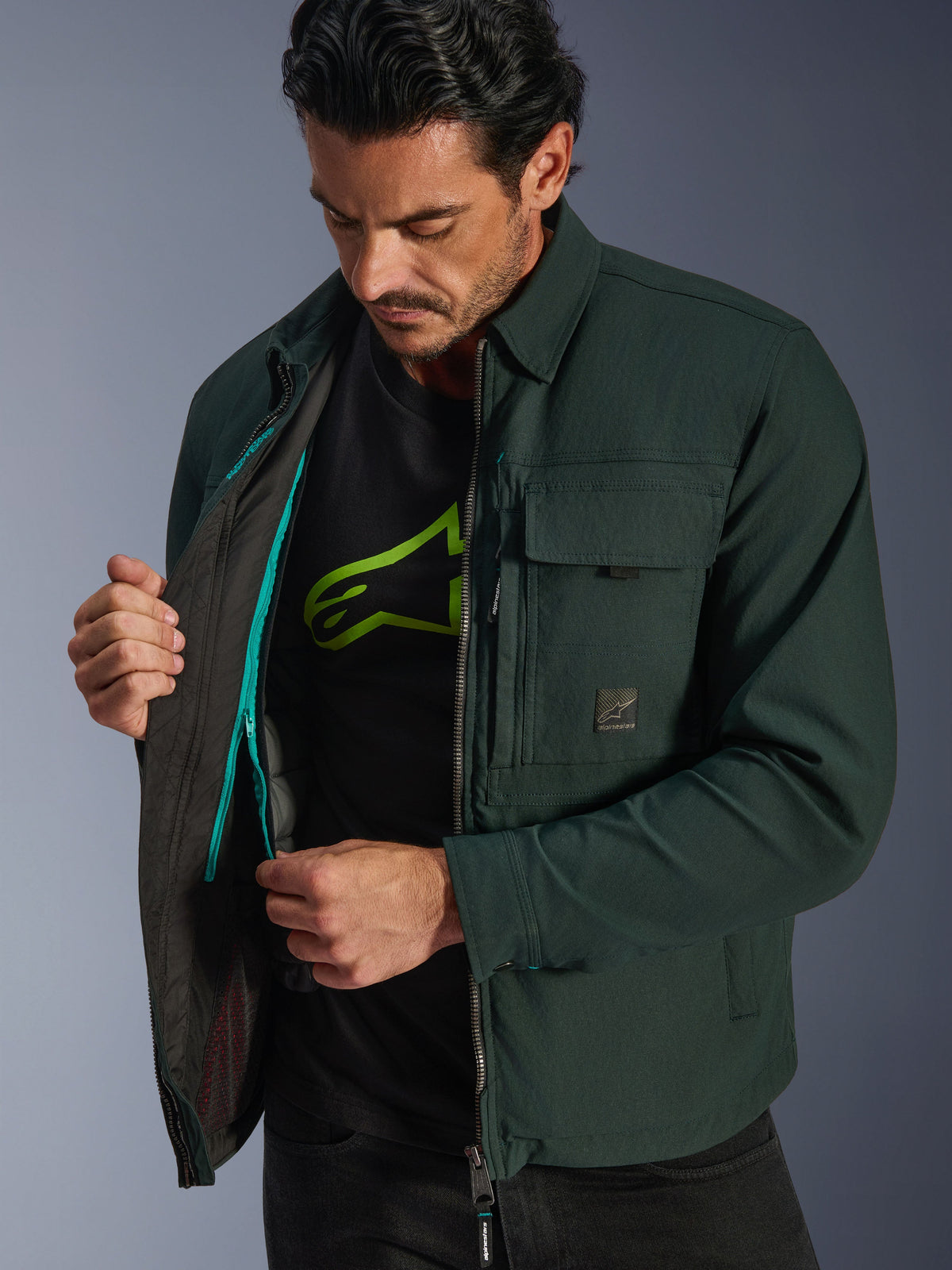 Alpinestars Bryon Water Resistant Overshirt, Dark Emerald, livsstilsbild av modell som visar den inre termovästen och den turkosa dragkedjedetaljen, urban motorcykeljacka i vaxad canvas med cargofickor
