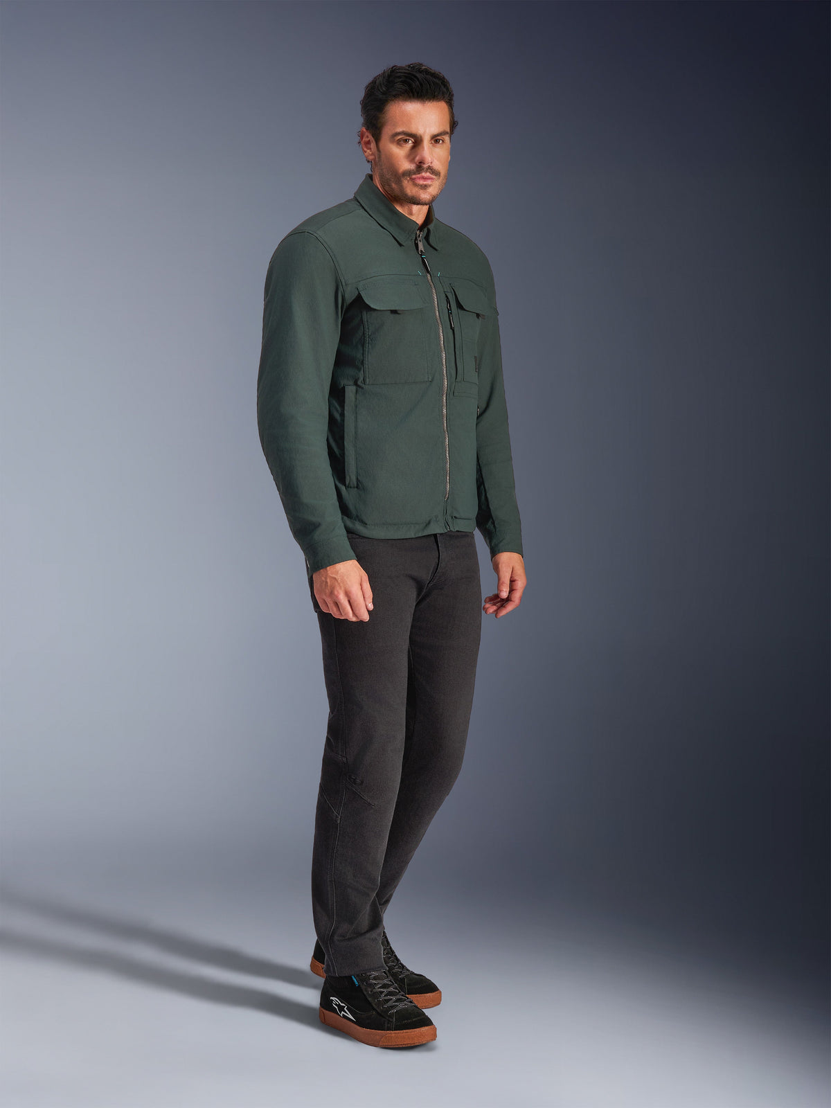 Alpinestars Bryon WR Overshirt, Dark Emerald motorcykeljacka, vattenavvisande vaxad canvas med cargofickor på bröstet och dragkedja framtill, bärs av en modell med mörka byxor och svarta sneakers, urban modern körutrustning