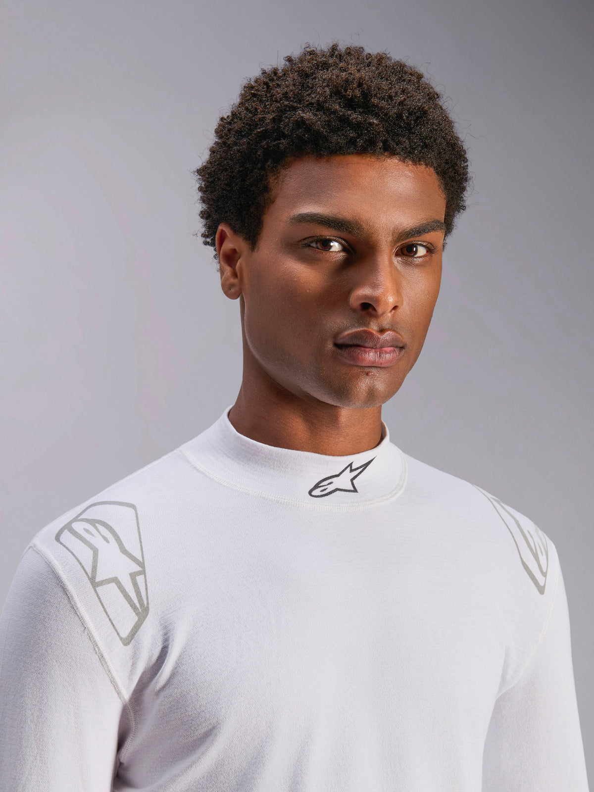 Alpinestars ZX Evo V3 Topp - Långärmad, vitt baslager för bilracing, bärs av en manlig modell, halvpolo med svart Alpinestars-logotyp, silvriga grafiska tryck på axlarna, lättviktigt flamskyddat motorsportunderställ