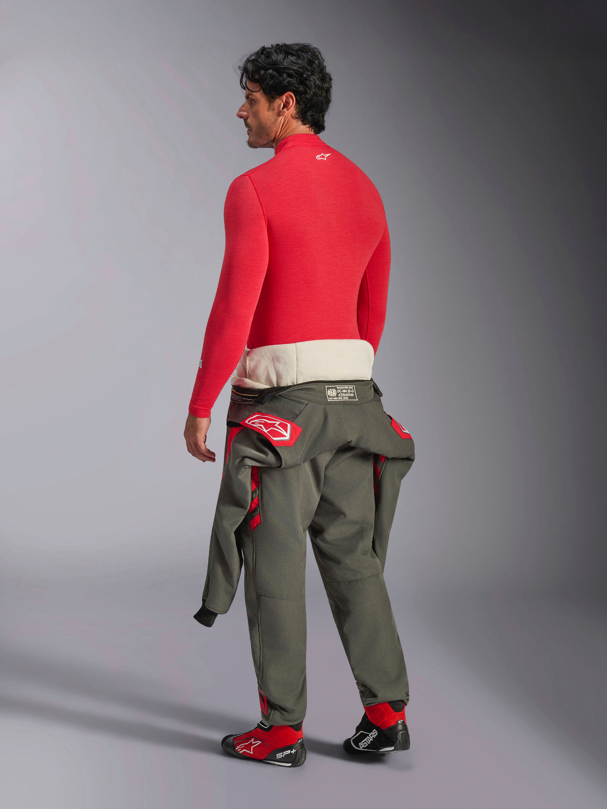 Alpinestars ZX Evo V3 Långärmad Topp, rött tekniskt underställ för bilracing, ryggvy på manlig modell som bär olivgröna racingbyxor neddragna till midjan och röda racingskor, flamskyddat underställ för motorsport