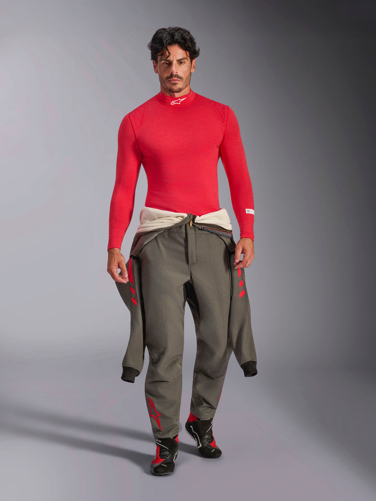 Alpinestars ZX Evo V3 Långärmad Top, rött underställ för bilracing, bärs av en modell med en grå racingdräkt knuten runt midjan och racingskor, mock neck med vit Alpinestars-logotyp, lätt och flamskyddad professionell motorsportutrustning