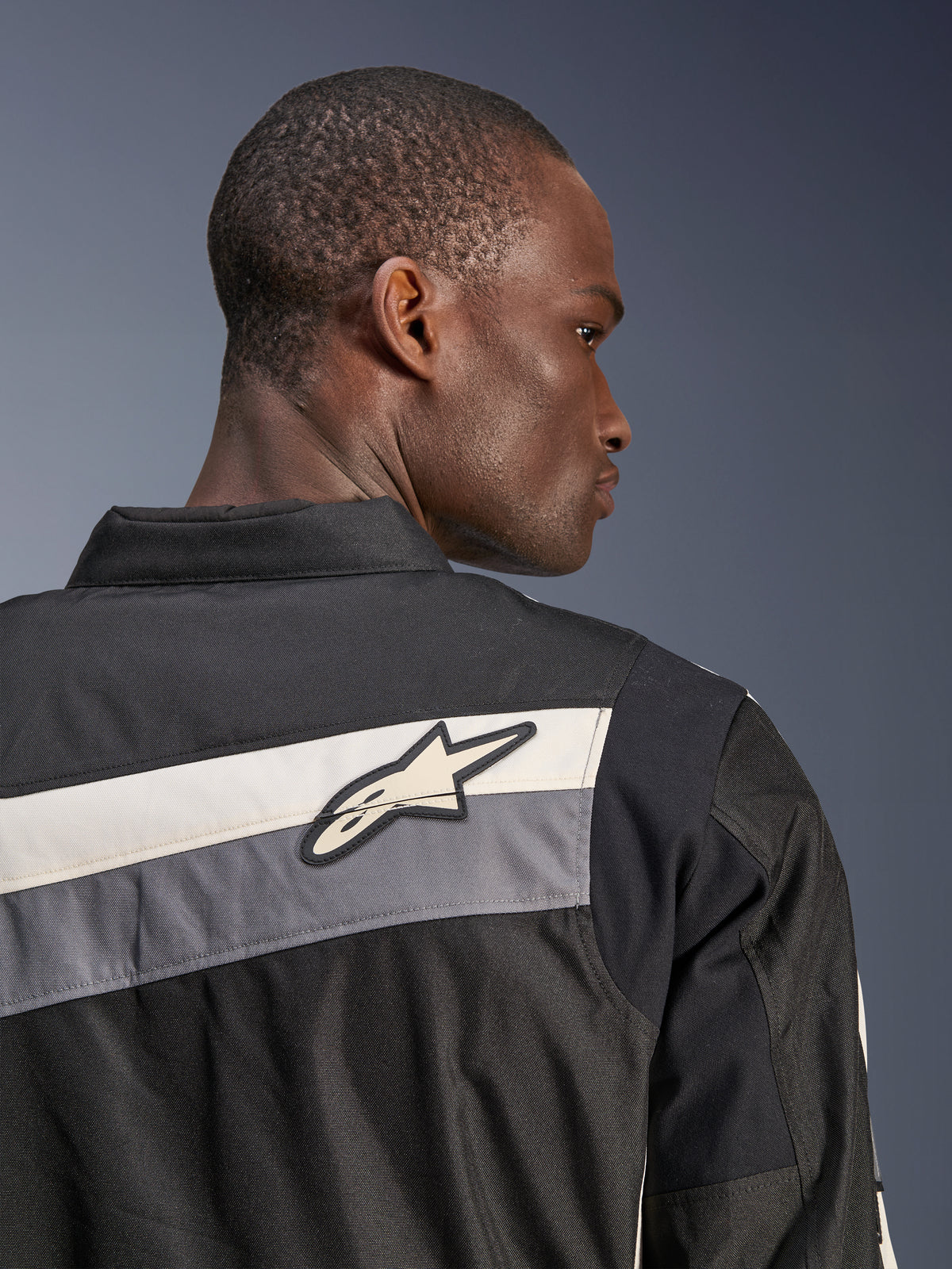 Alpinestars T-Dyno WR Jacket, Textile Motorcycle Jacket, Black Dark Gray and Ecru, close-up of the upper back and shoulder with horizontal stripes and Alpinestars star logo, worn by a model, heritage-inspired design for road riding