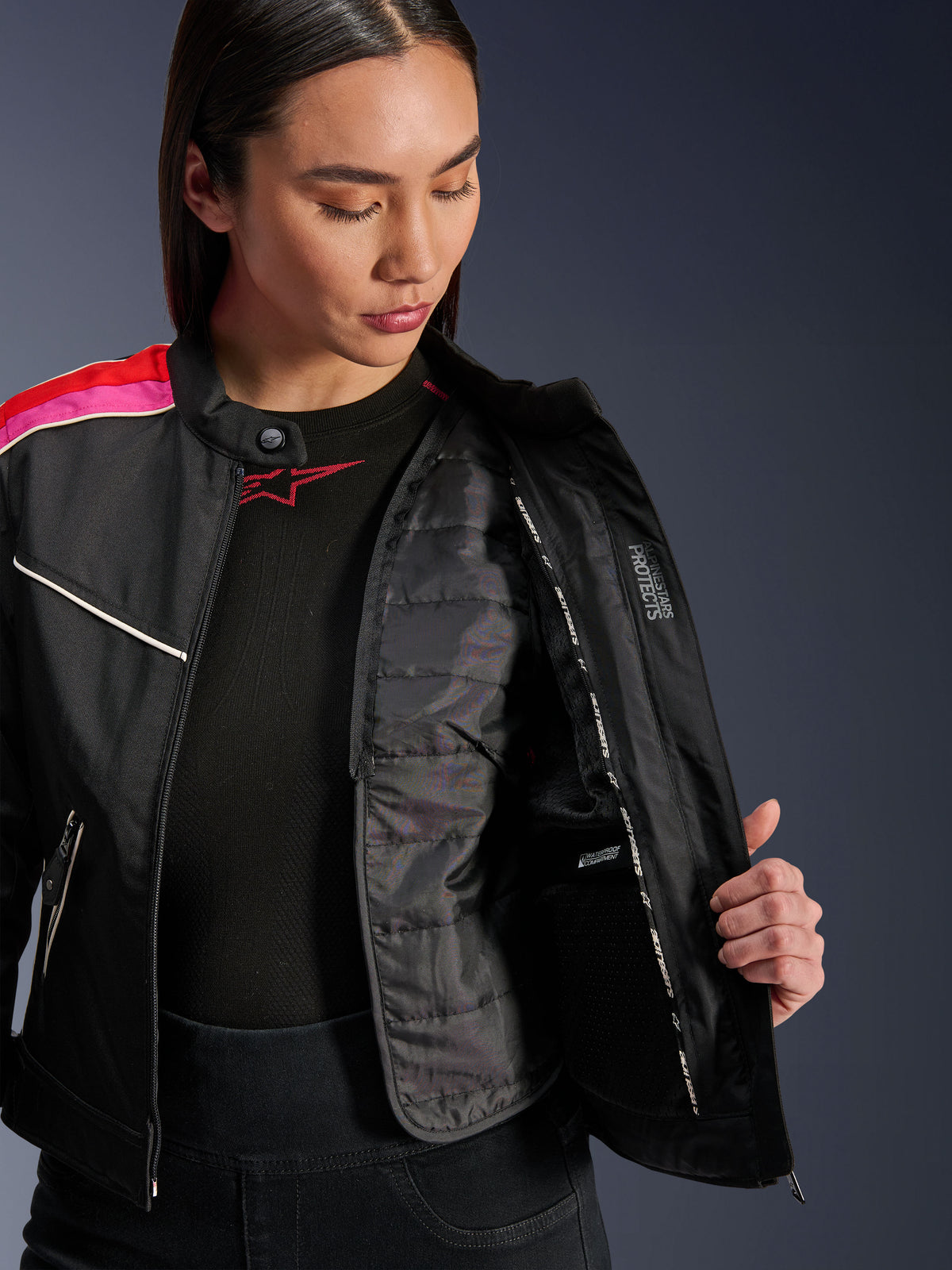 Alpinestars Stella T-Dyno WR Jacka, textilmotorcykeljacka i svart, ljusröd och fuchsia, öppnad för att visa den invändiga kviltade termovästen och den vattentäta fickan, vintageinspirerad biker-passform för dam