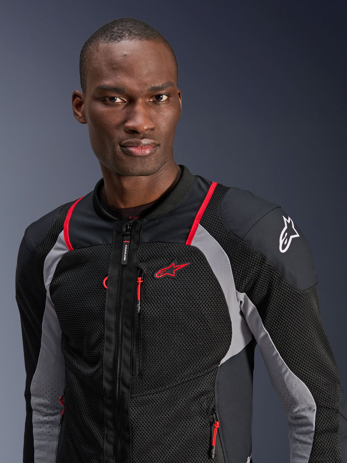 Man i Alpinestars Troop-Air Pro-jacka, svart, askgrå och klarröd, teknisk bepansrad luftjacka med ventilerande meshpaneler, röda detaljer och Alpinestars-logotyp på axeln, urban samtida motorcykelutrustning