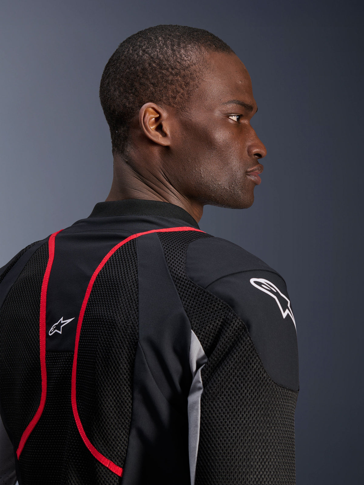 Alpinestars Troop-Air Pro-jacka, teknisk bepansrad ventilerad jacka, svart, askgrå och klarröd, närbild i profil och bakifrån som visar meshpaneler i textil, röda detaljer och vita Astars-logotyper på axeln och övre delen av ryggen