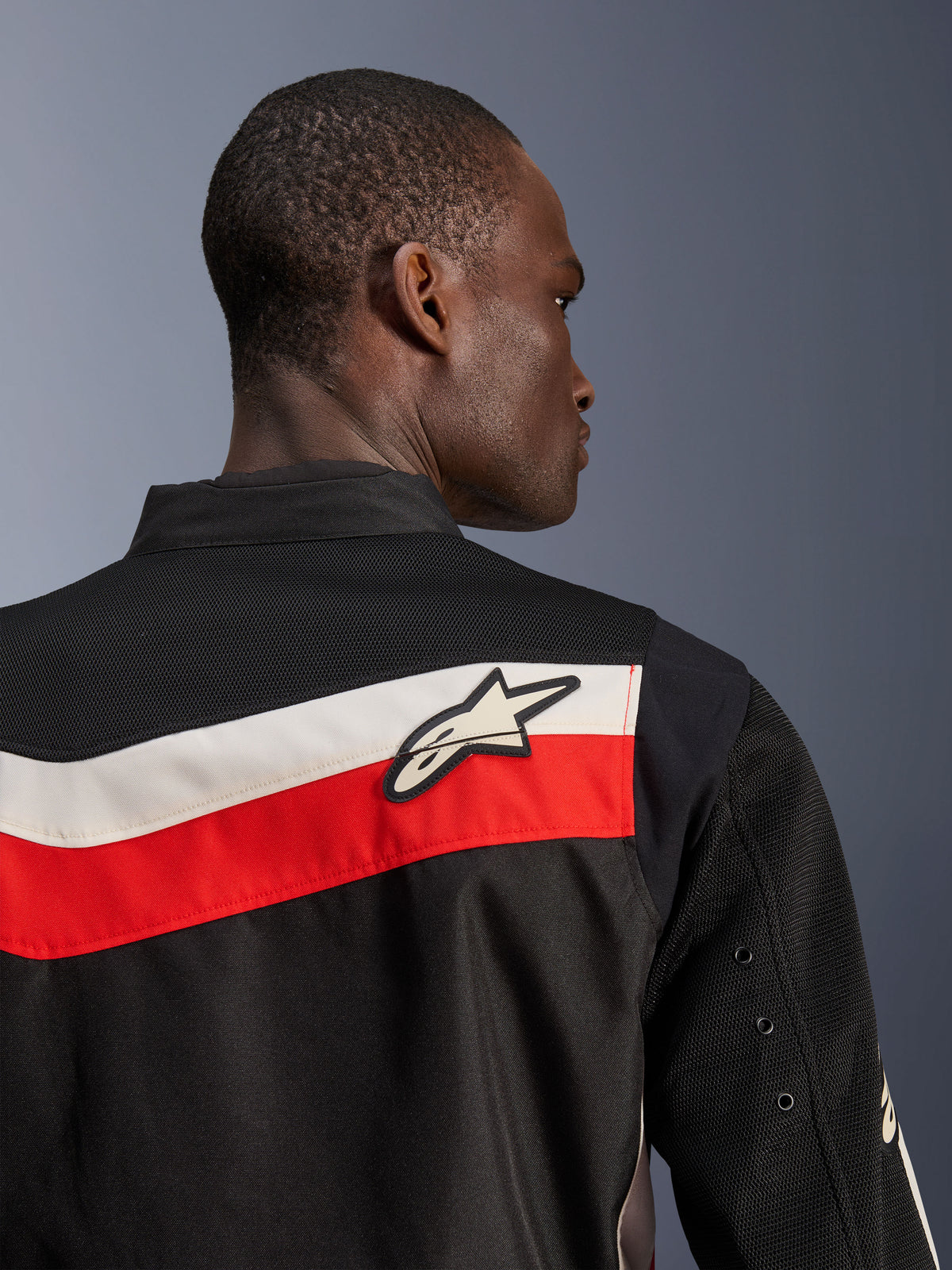 Alpinestars T-Dyno Air Jacket, svart, klarröd och ecru, närbild av övre rygg och axel, horisontella röda och ecru-färgade ränder med en vit Astars-logotyp, ventilerande 3D-meshpaneler på oket och ärmarna, modern klassisk motorcykeljacka i textil