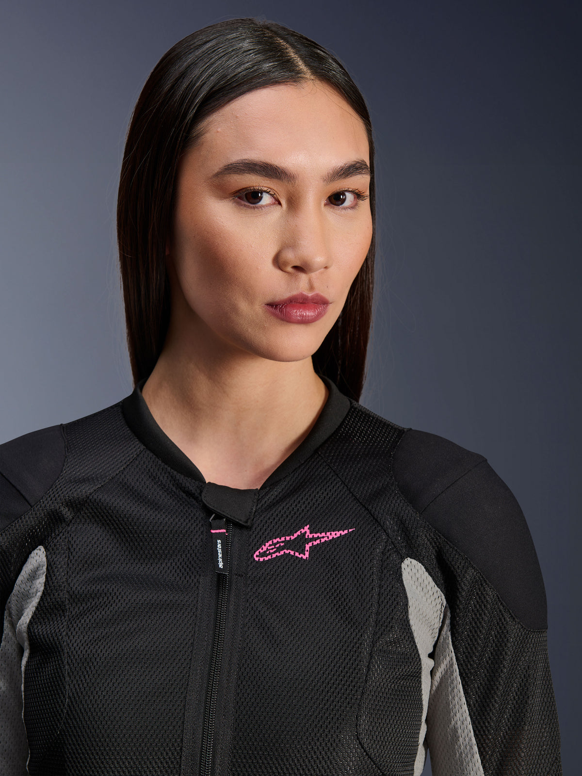 Kvinna som bär Alpinestars Stella Troop-Air-jacka, Black Ash Gray och Pink Fluo, närbild som framhäver den tekniska mesh-konstruktionen och den rosa logotypen på bröstet, stilren urban motorcykelutrustning