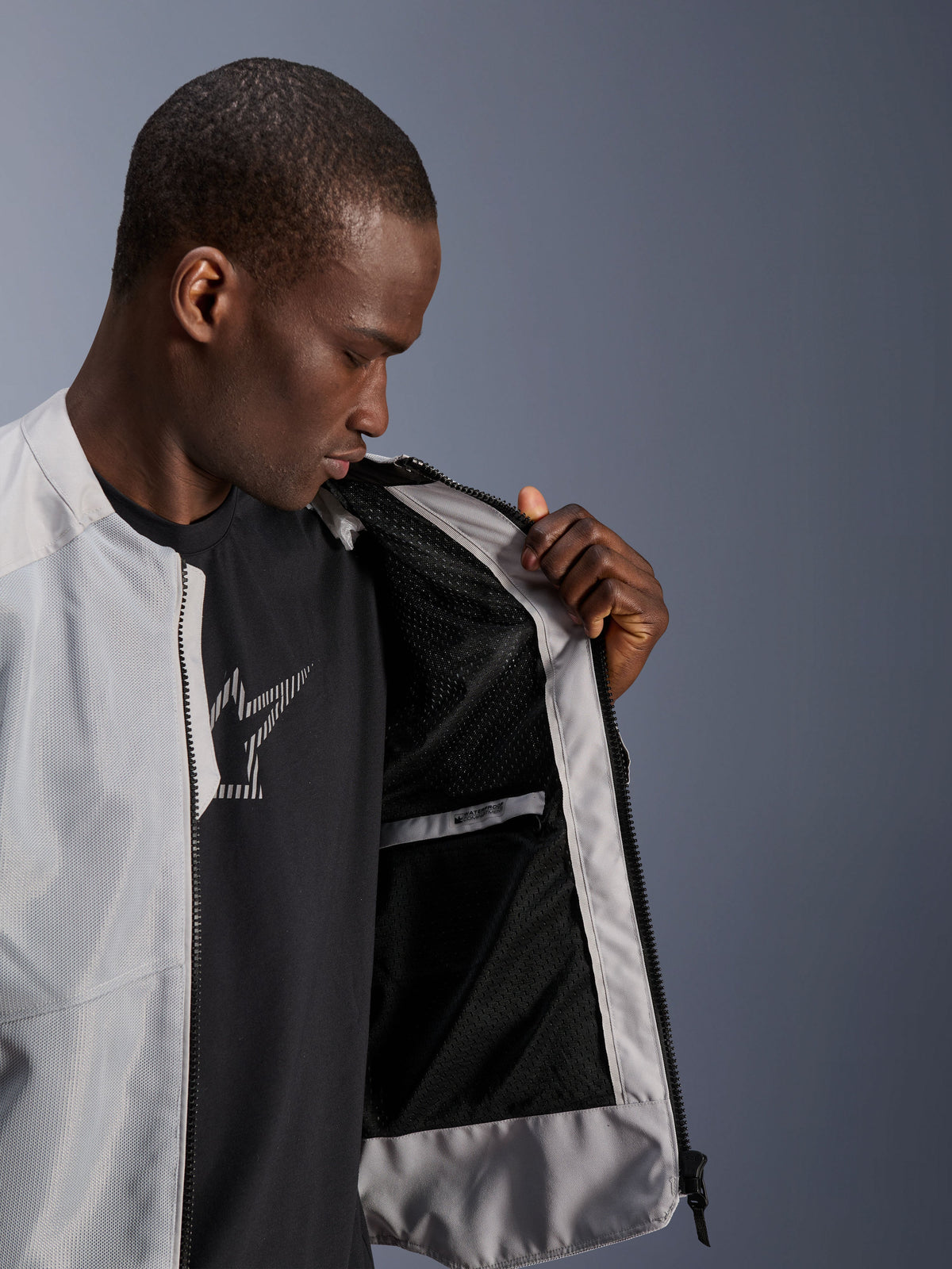 Manlig modell bär Alpinestars C-1 Air-jacka i Silver, öppnar framsidan för att visa det svarta tekniska mesh-innerfodret och en vattentät innerficka med dragkedja.