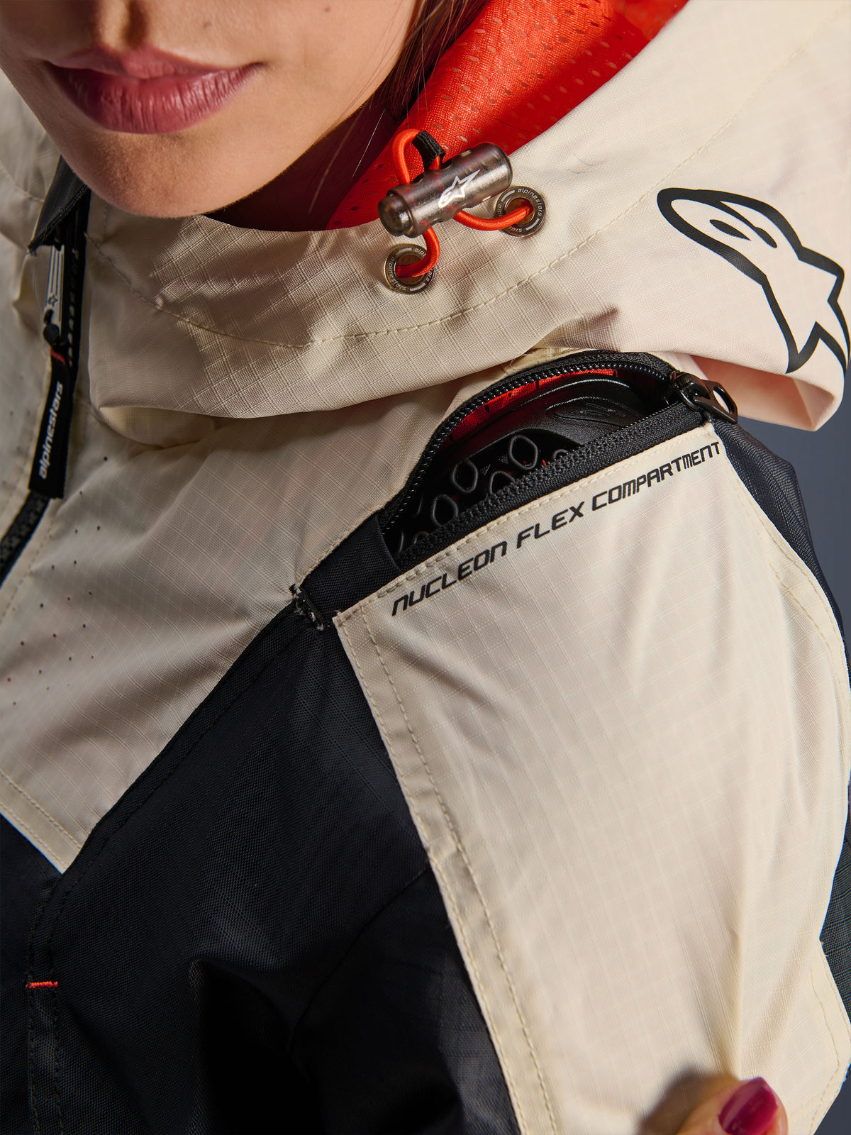 Alpinestars Molly Air jacka, motorcykeljacka dam, Black Almond, närbild på axeln som visar dragkedjan för Nucleon Flex-facket, ripstop-tyg och orange nätfoder inuti huvan