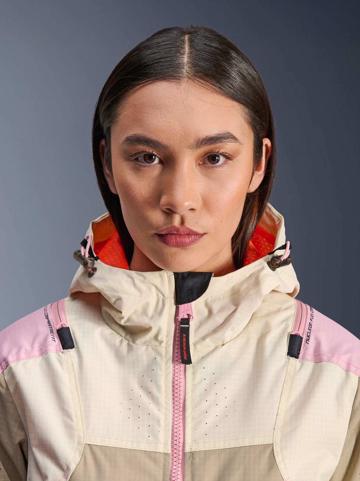 Närbild på en kvinnlig modell som bär Alpinestars Molly Air Jacket i Sand Pink Almond, hög krage och huva med klarorange foder, rosa dragkedja framtill, ripstop-tyg med laserperforerat bröst för ventilation, urban skyddsutrustning för motorcykel