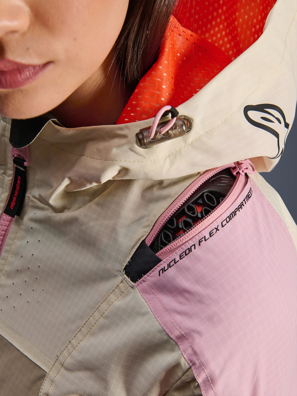 Närbild på Alpinestars Molly Air Jacket i Sand Pink Almond som visar det dragkedjeförsedda axelfacket för Nucleon Flex-skydd, det klarorangea nätfodret i huvan och den slitstarka ripstop-konstruktionen.